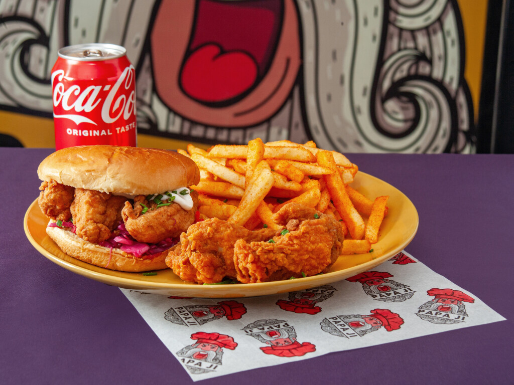 A vibrant yellow plate showcases crispy fried chicken sandwich, spicy fries, and a cold Coca-Cola in a lively, colorful setting.