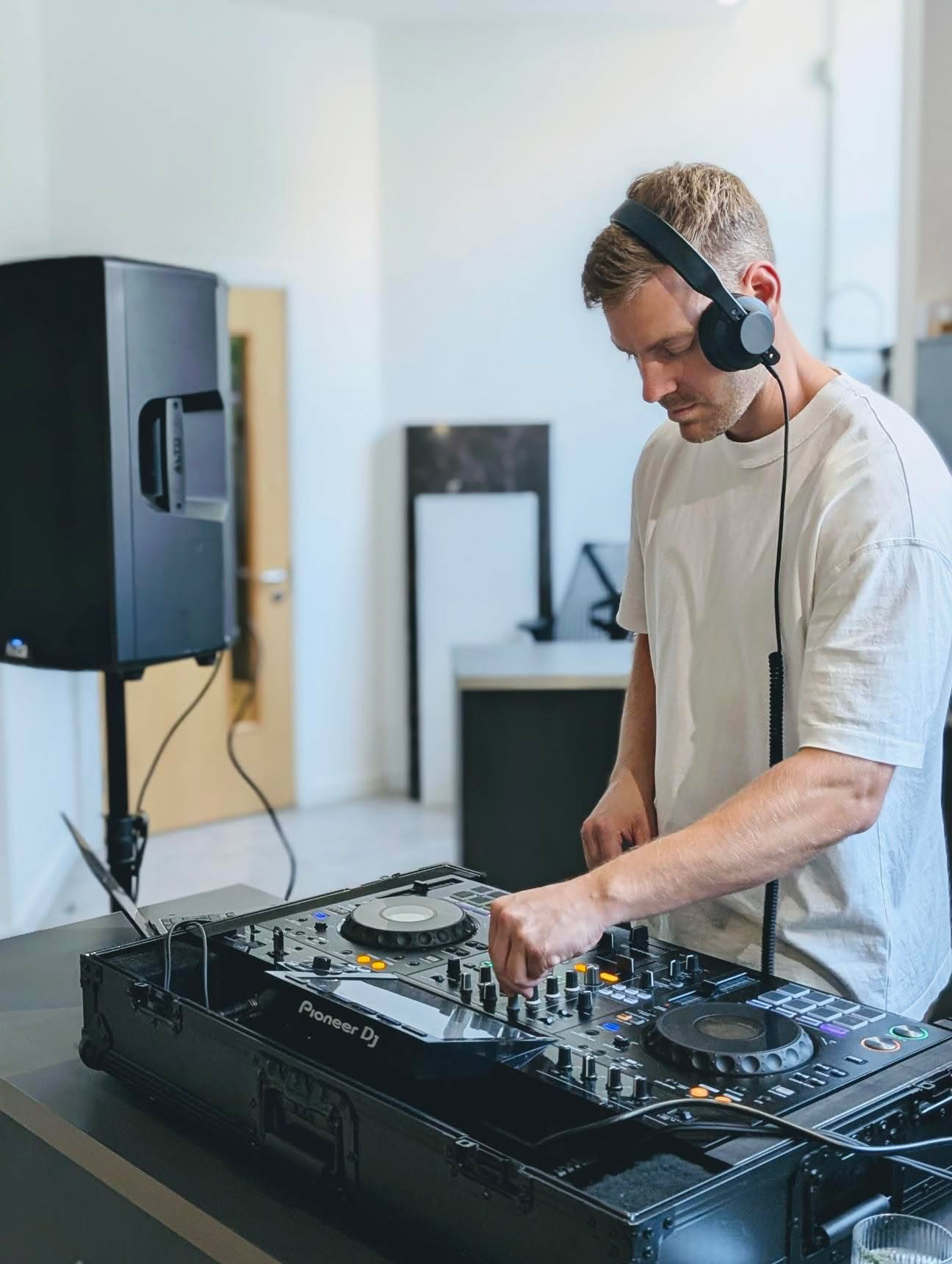 A DJ in a minimalistic space focuses on a sleek Pioneer controller, with DJ equipment gleaming under bright daylight, creating a vibrant atmosphere.