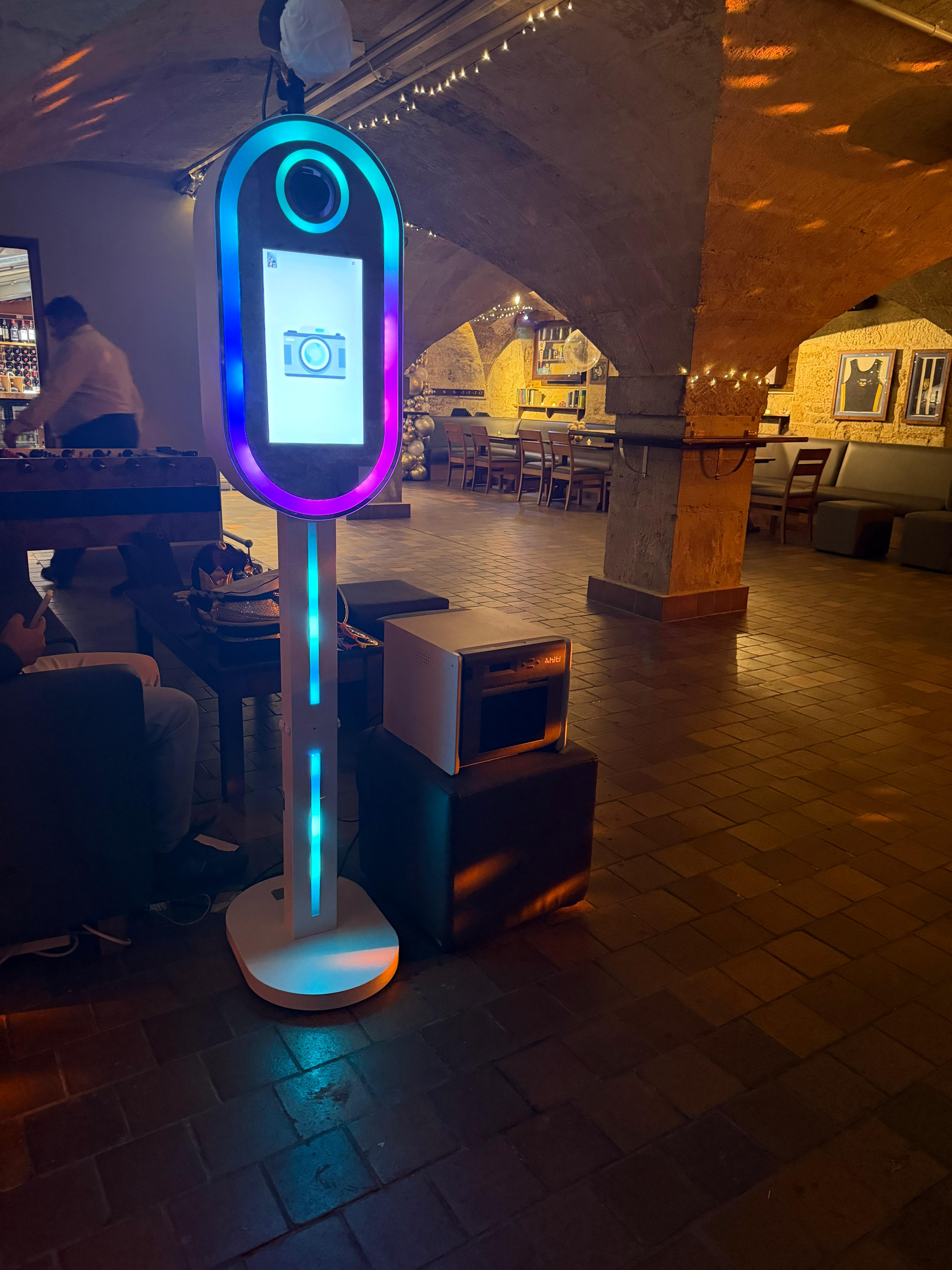 A vibrant photo booth with colorful lights stands in a cozy, dimly-lit venue featuring rustic stone arches, enhancing the festive atmosphere.