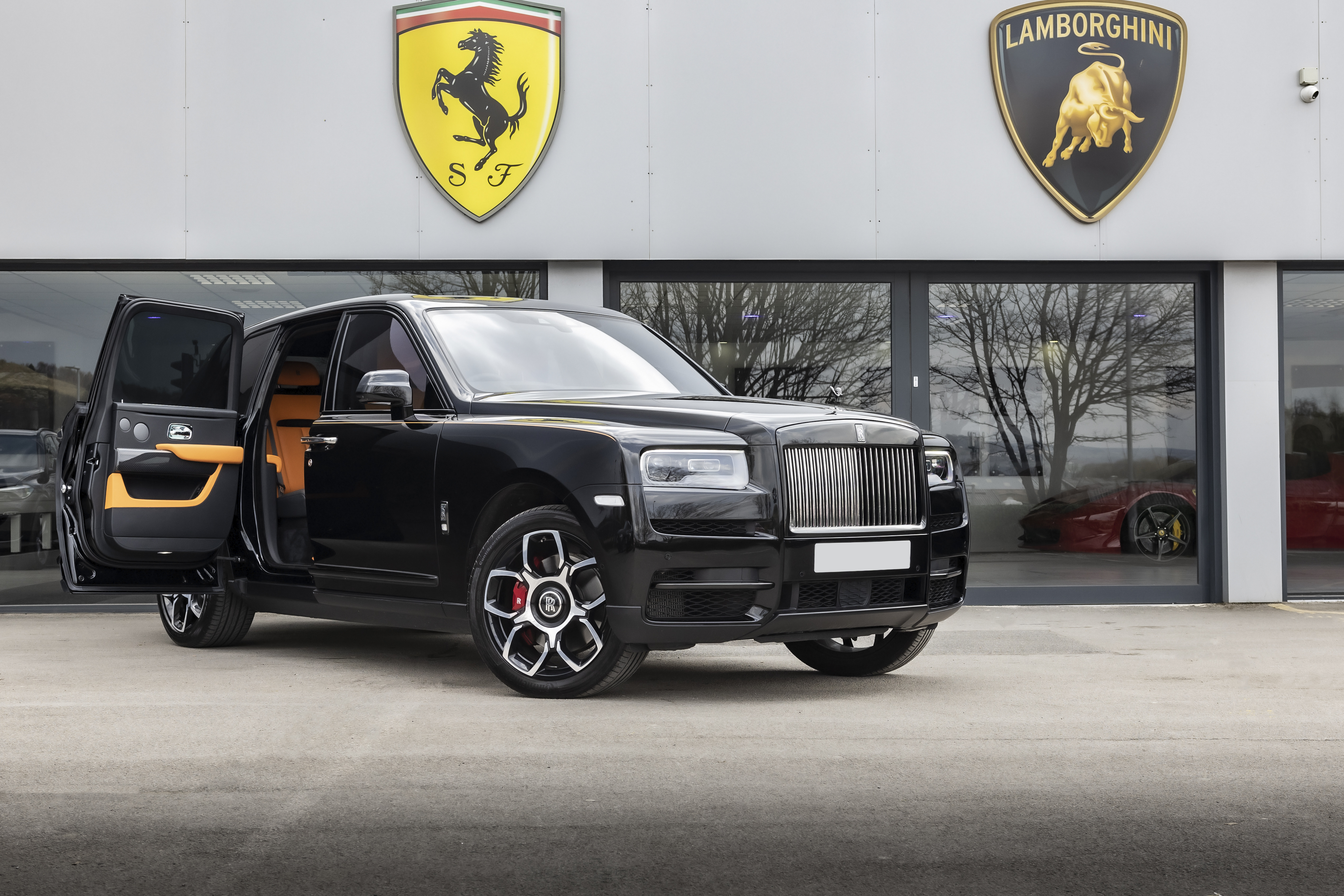 A sleek black Rolls-Royce with vibrant orange accents stands next to a luxury showroom, projecting an aura of opulence and style.