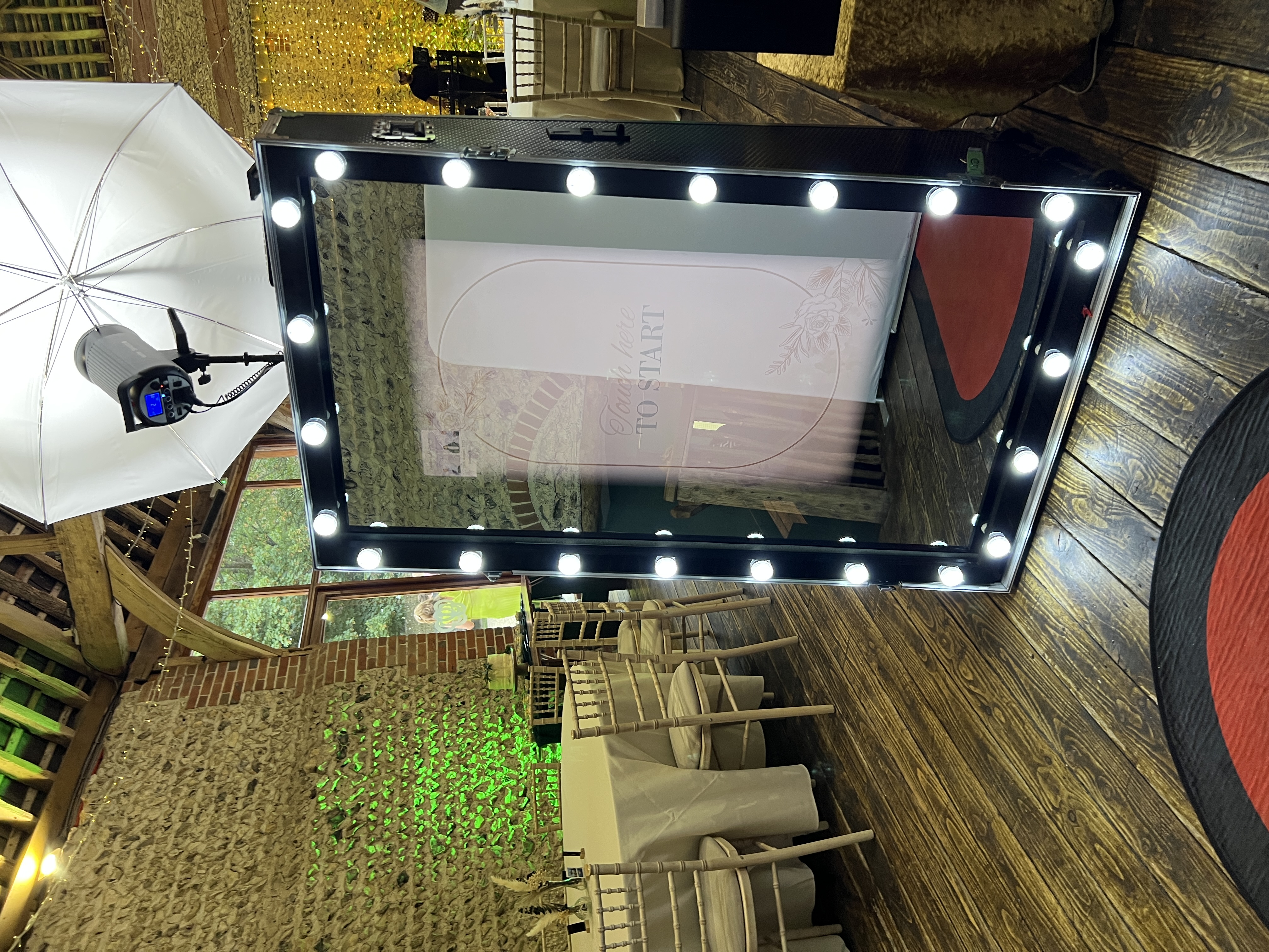 A stylish photo booth with bright lights reflects a welcoming atmosphere, set against rustic wooden floors and elegant beige table settings.