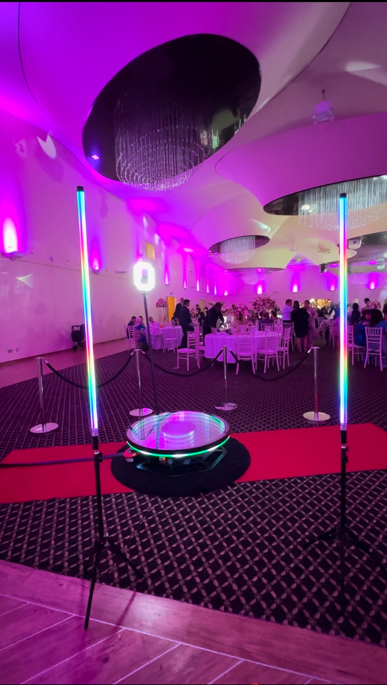 A vibrant event space featuring pink lighting and elegant white tables adorned with floral centerpieces, creating a festive atmosphere.