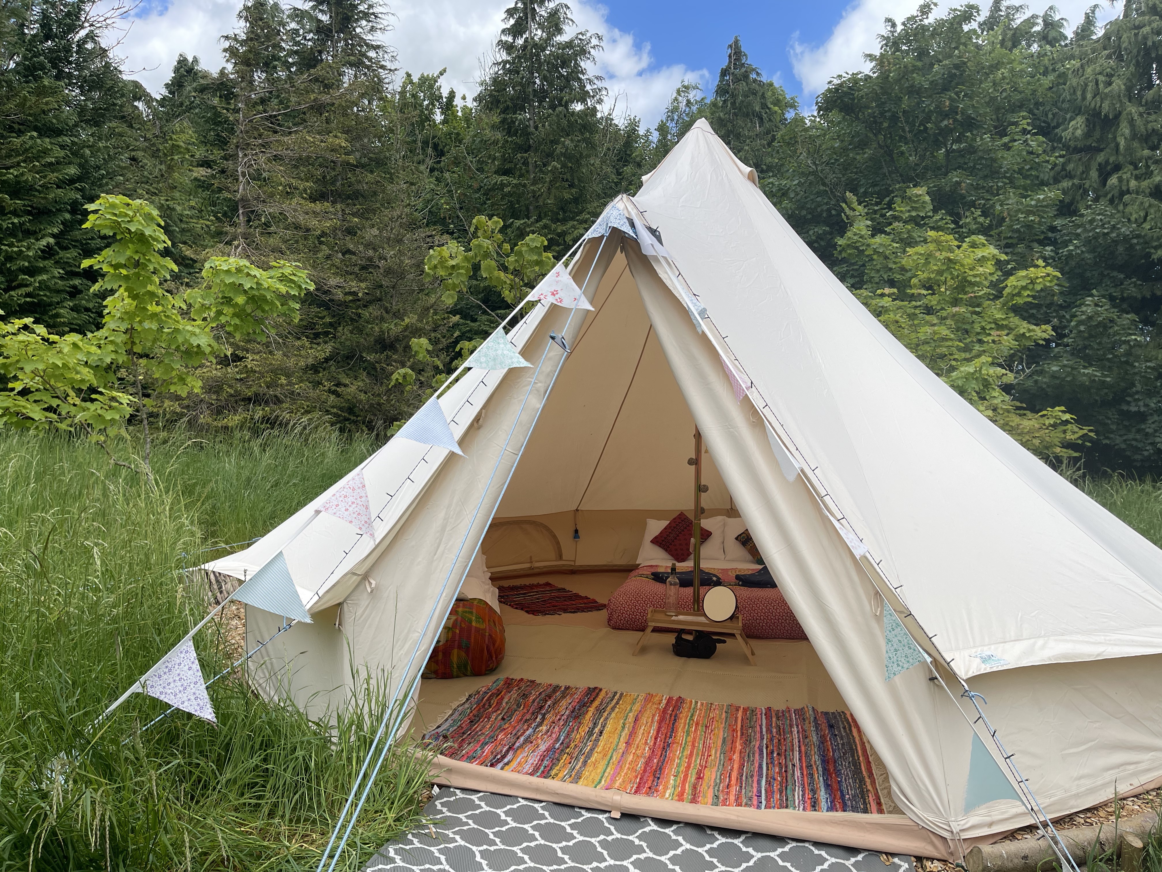 A cozy glamping tent features vibrant patterned rugs, a plush bean bag, and decorative bunting, all set under soft, natural light.