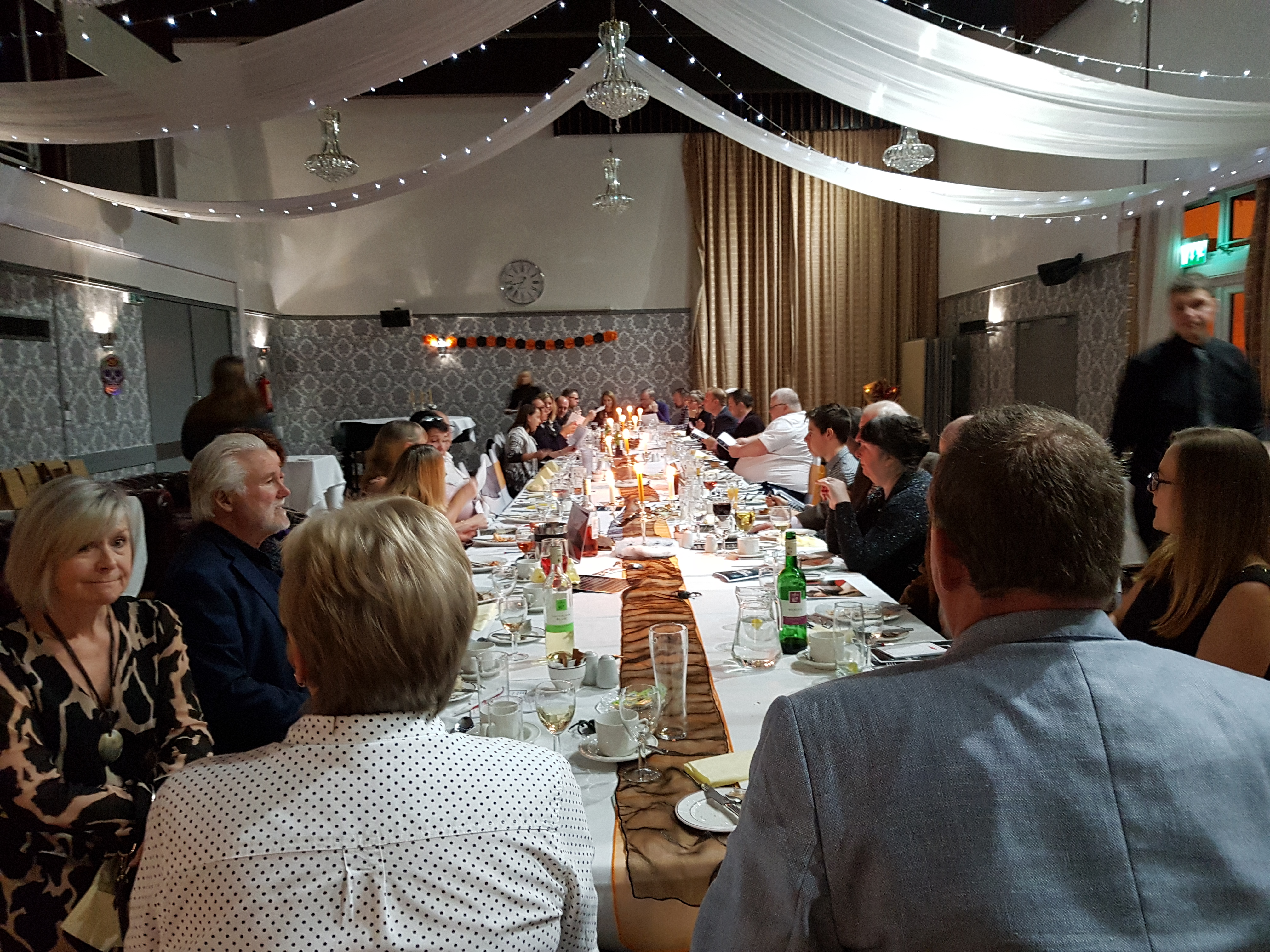 A long banquet table adorned with crisp linen and flickering candles, surrounded by elegantly dressed guests enjoying a warm, festive atmosphere.