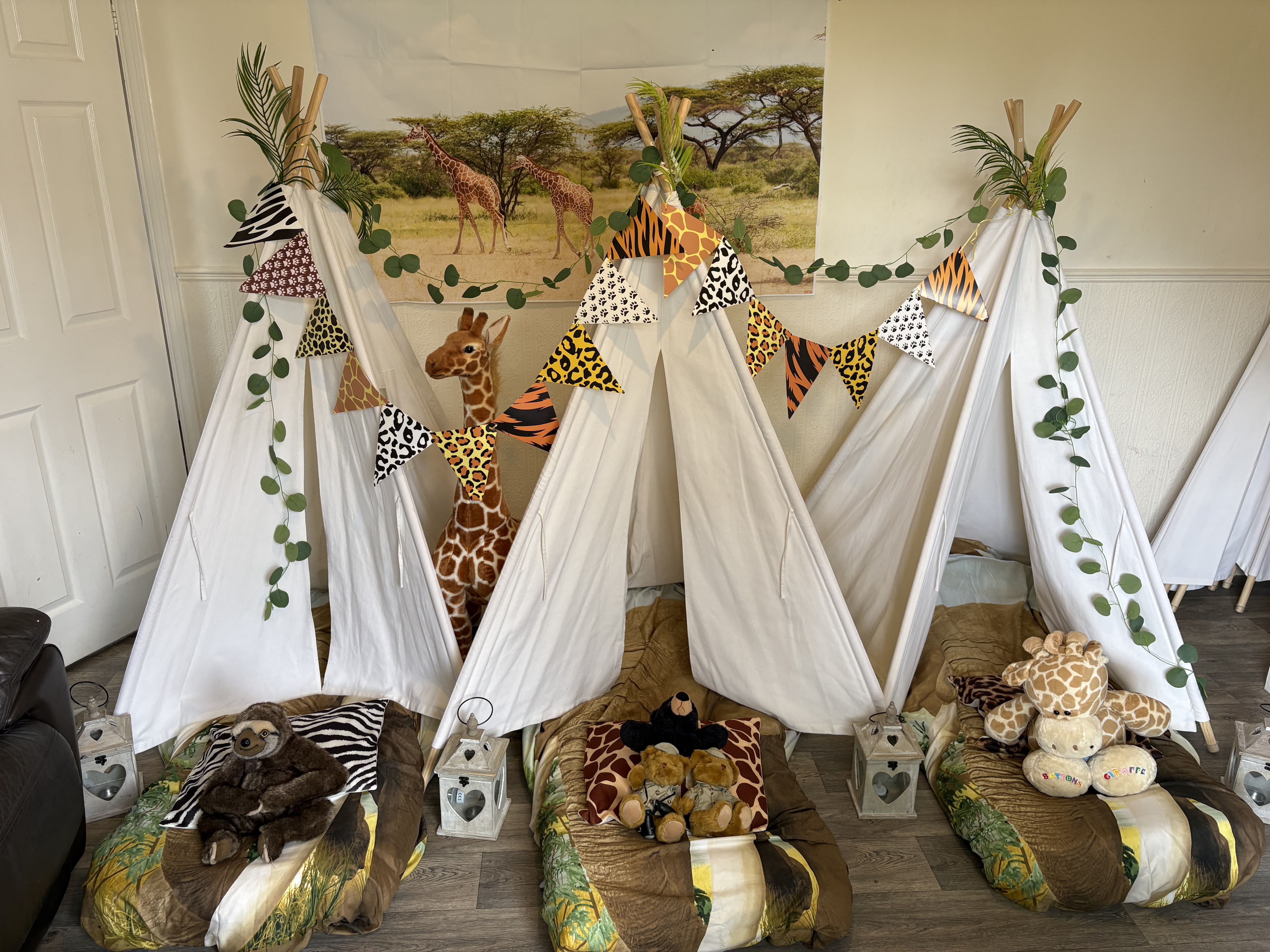 Safari-themed teepee sleepover with white tents, plush giraffes, lanterns, green garlands, and bold animal-print bunting on a cozy floor setup.