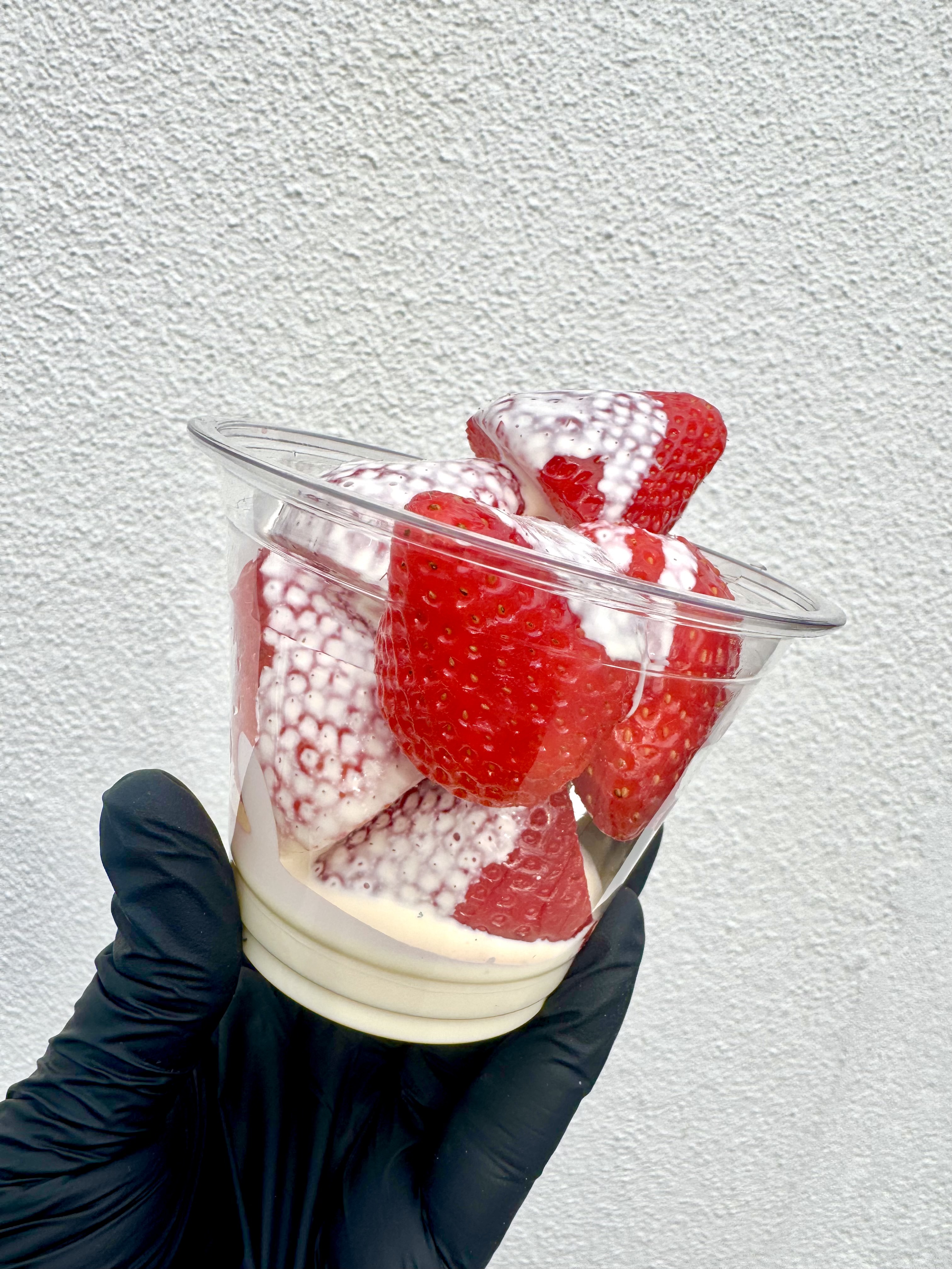 Vibrant strawberries nestled in a white paper cup, accented with delicate edible flowers, evoke a fresh, inviting atmosphere for catering.