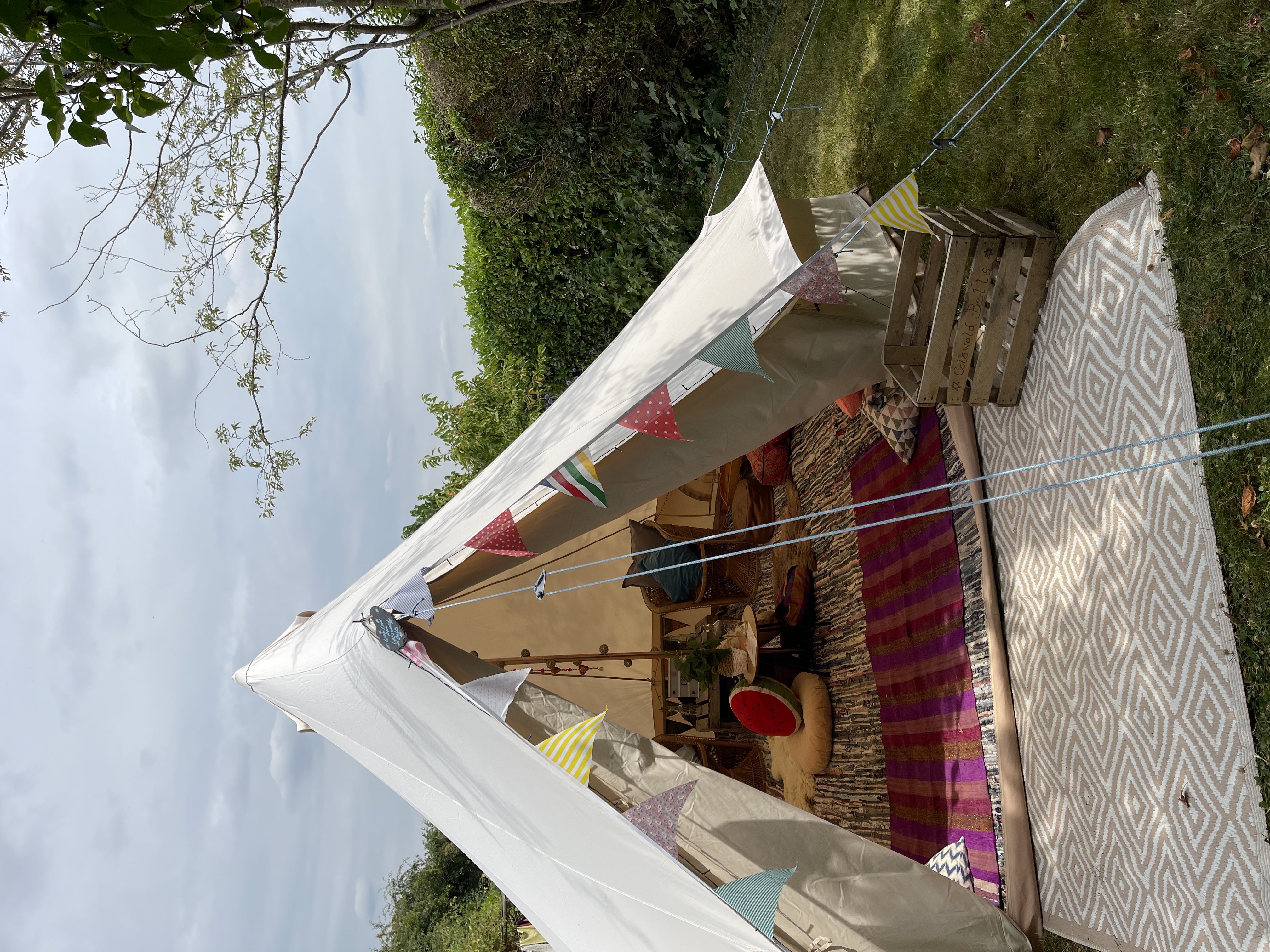 A cozy outdoor tent adorned with colorful bunting, featuring layered rugs and a low table surrounded by plush cushions, creating a relaxed vibe.