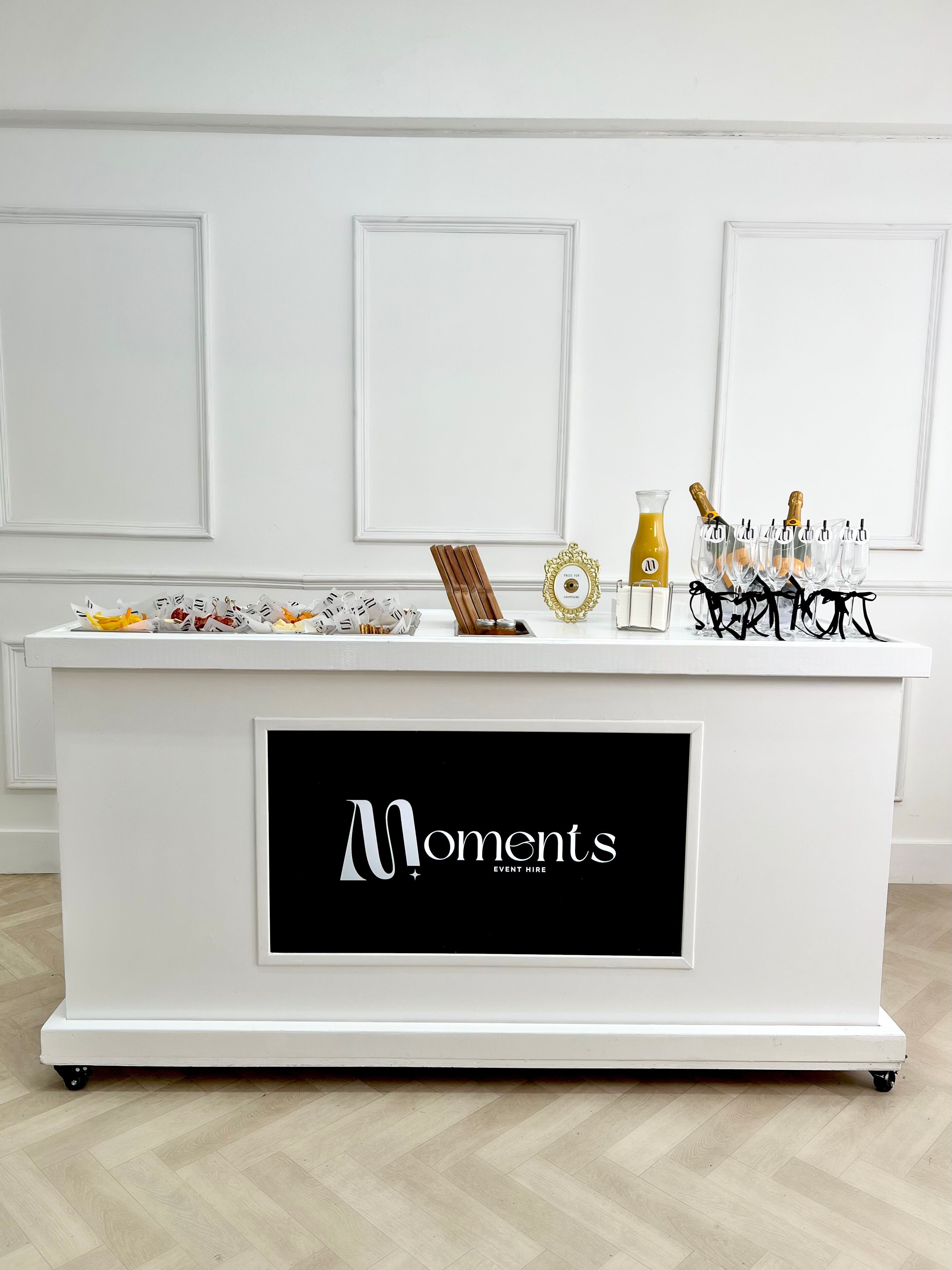 A sleek white catering table displays vibrant fruits and elegant glassware, exuding sophistication in bright, inviting light.
