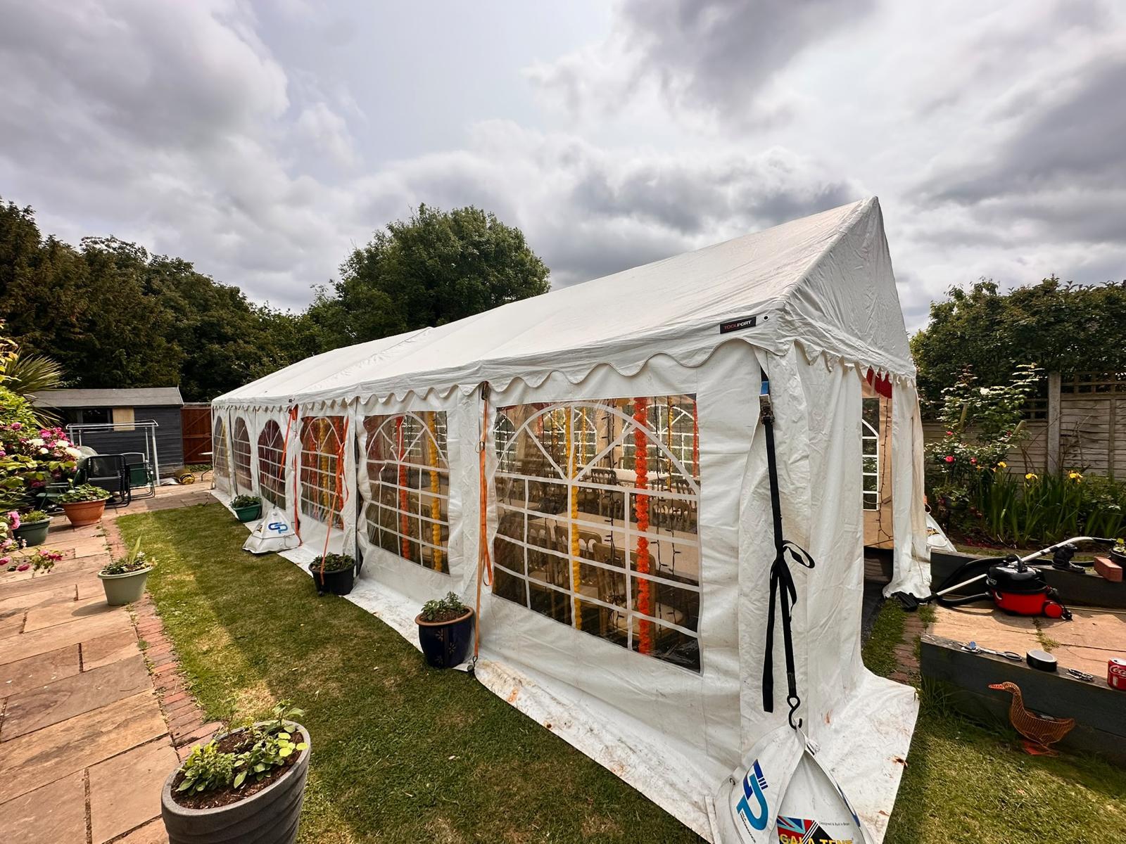 A white marquee tent houses vibrant floral decor outside, equipped for events, illuminated by soft daylight, enhancing a cozy atmosphere.