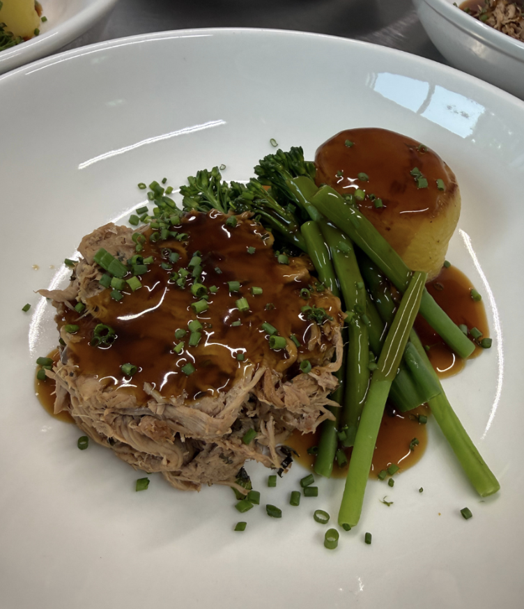 Pulled pork with glossy brown gravy, green asparagus and broccolini, plus a glazed potato on a white plate; polished catering presentation.