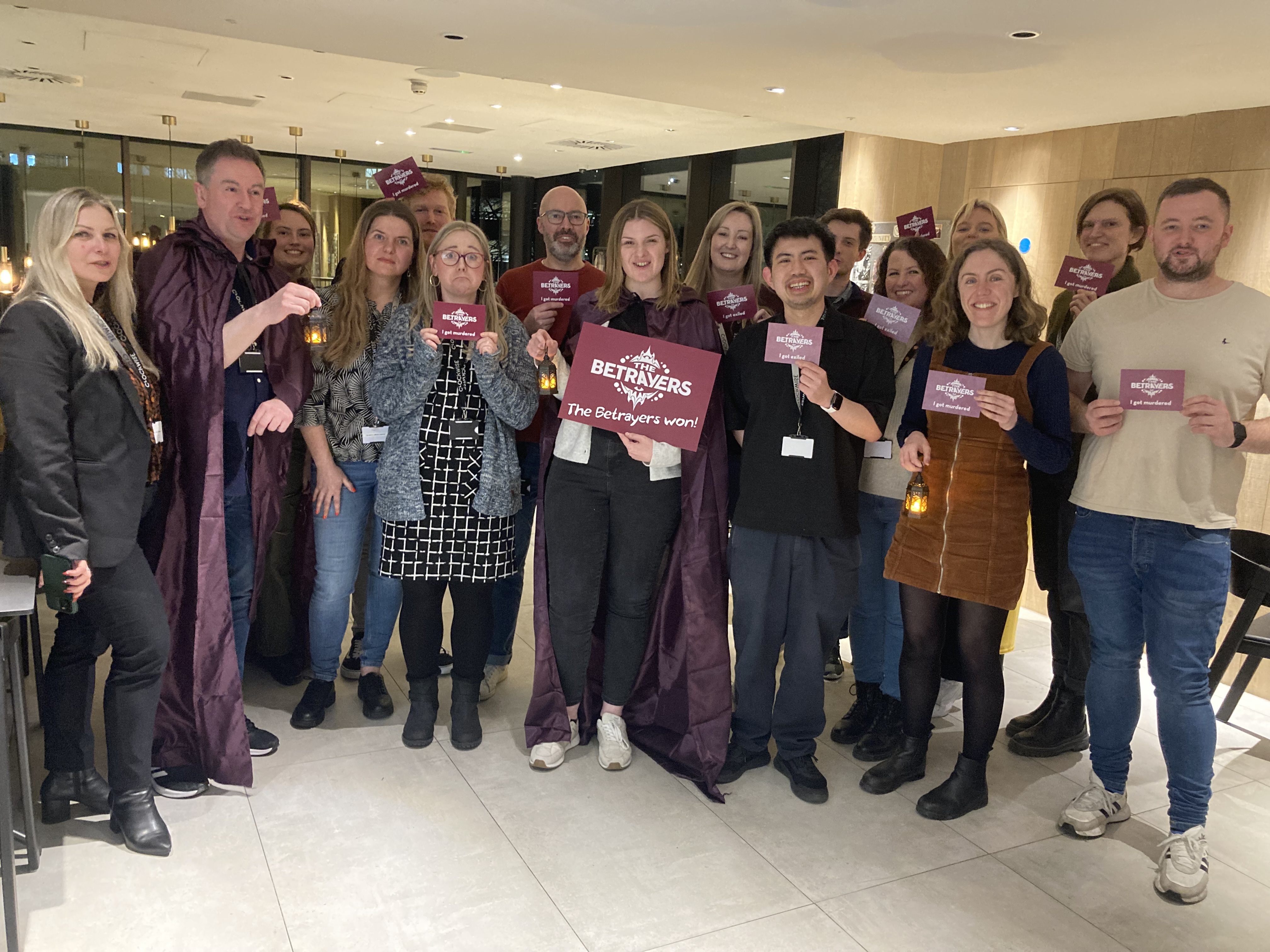 A cheerful group in stylish attire, holding signs, radiates positive energy in a modern setting with softly glowing light fixtures.