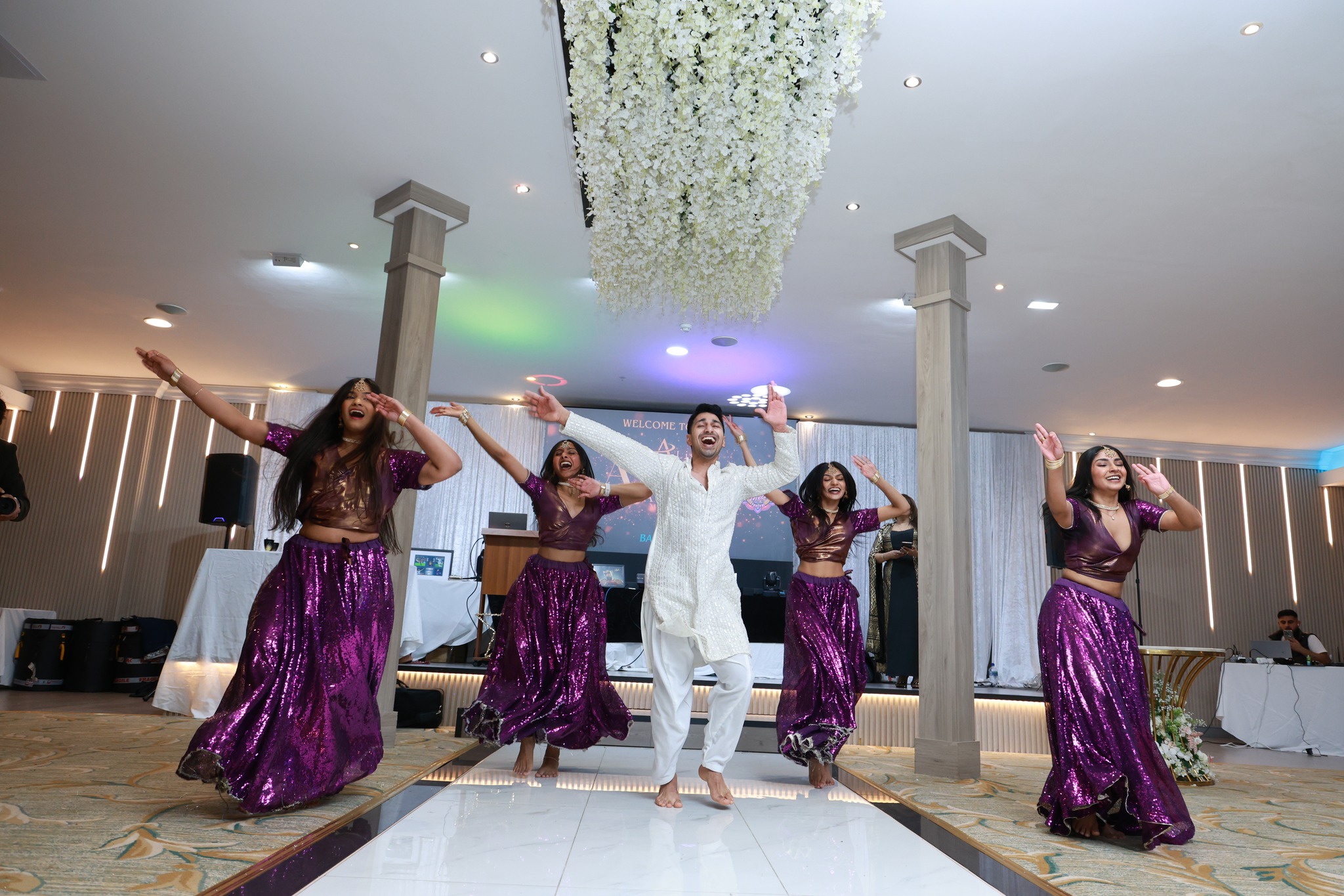 A vibrant dance scene features performers in shimmering purple outfits moving energetically on a polished floor, under warm lighting.