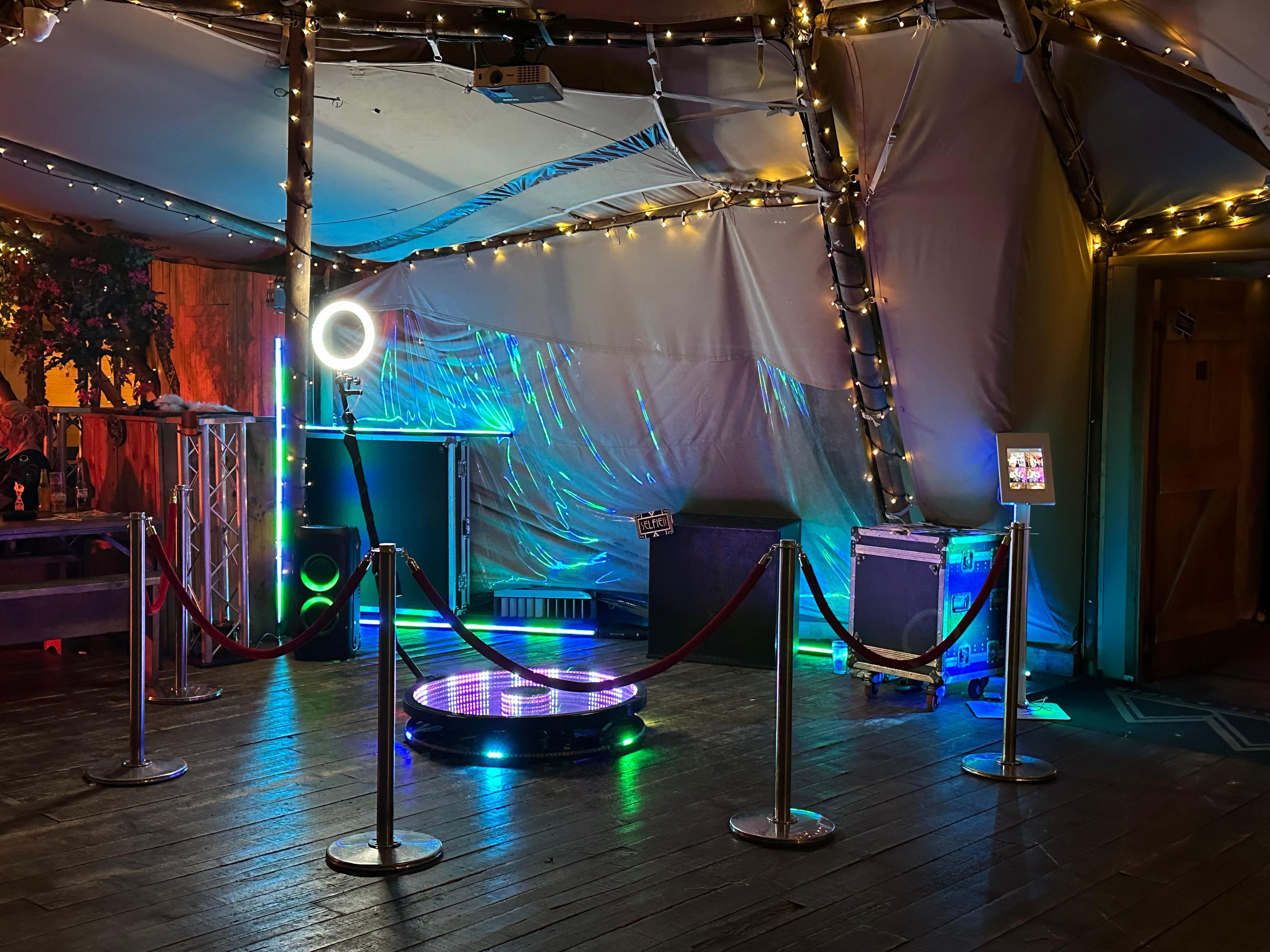 A vibrant event space showcases a circular illuminated dance floor, surrounded by velvet ropes and colorful LED lights, creating a festive atmosphere.