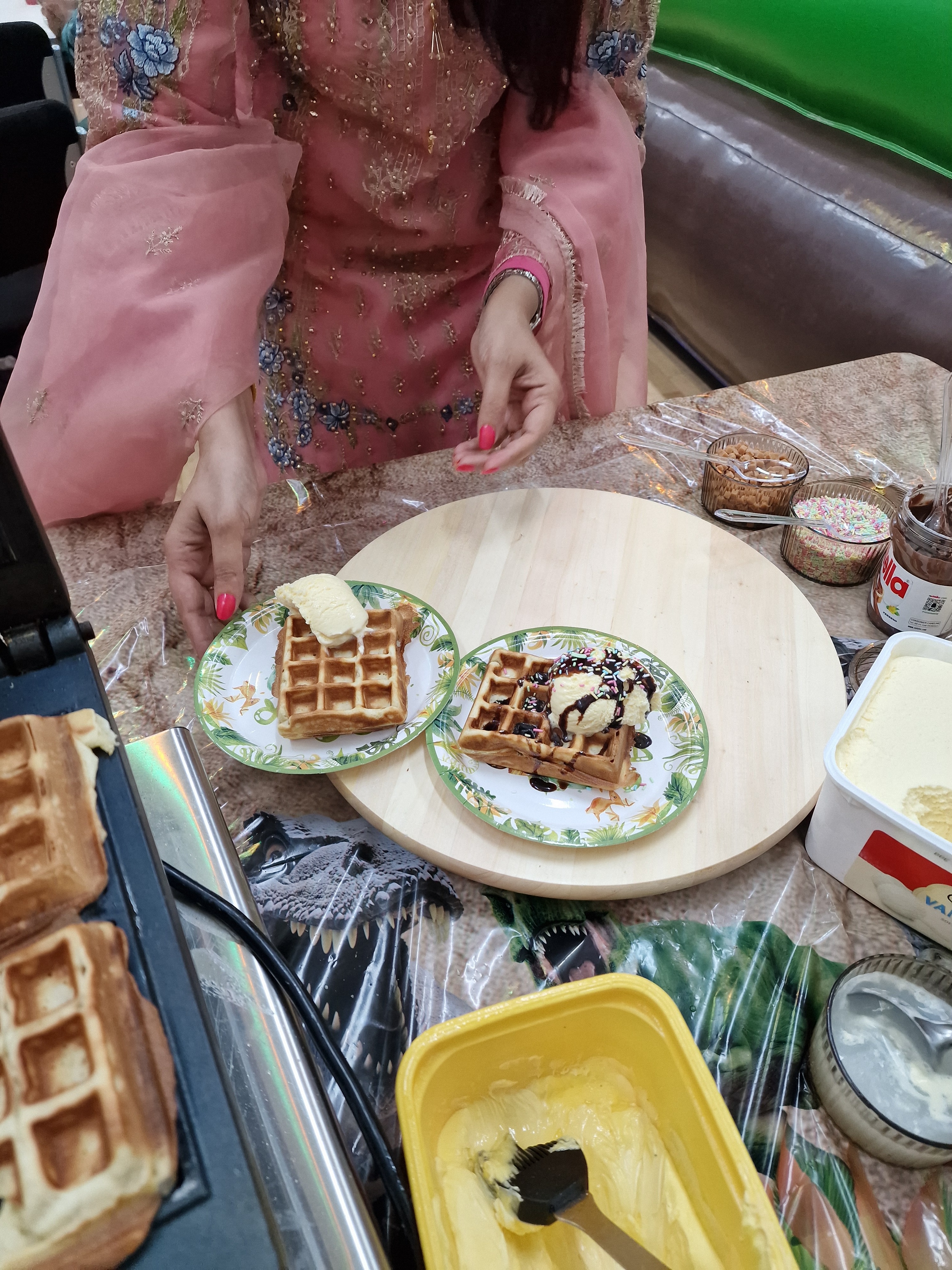 Golden waffles topped with creamy ice cream and chocolate sauce are arranged on decorative plates atop a playful dinosaur-themed table.