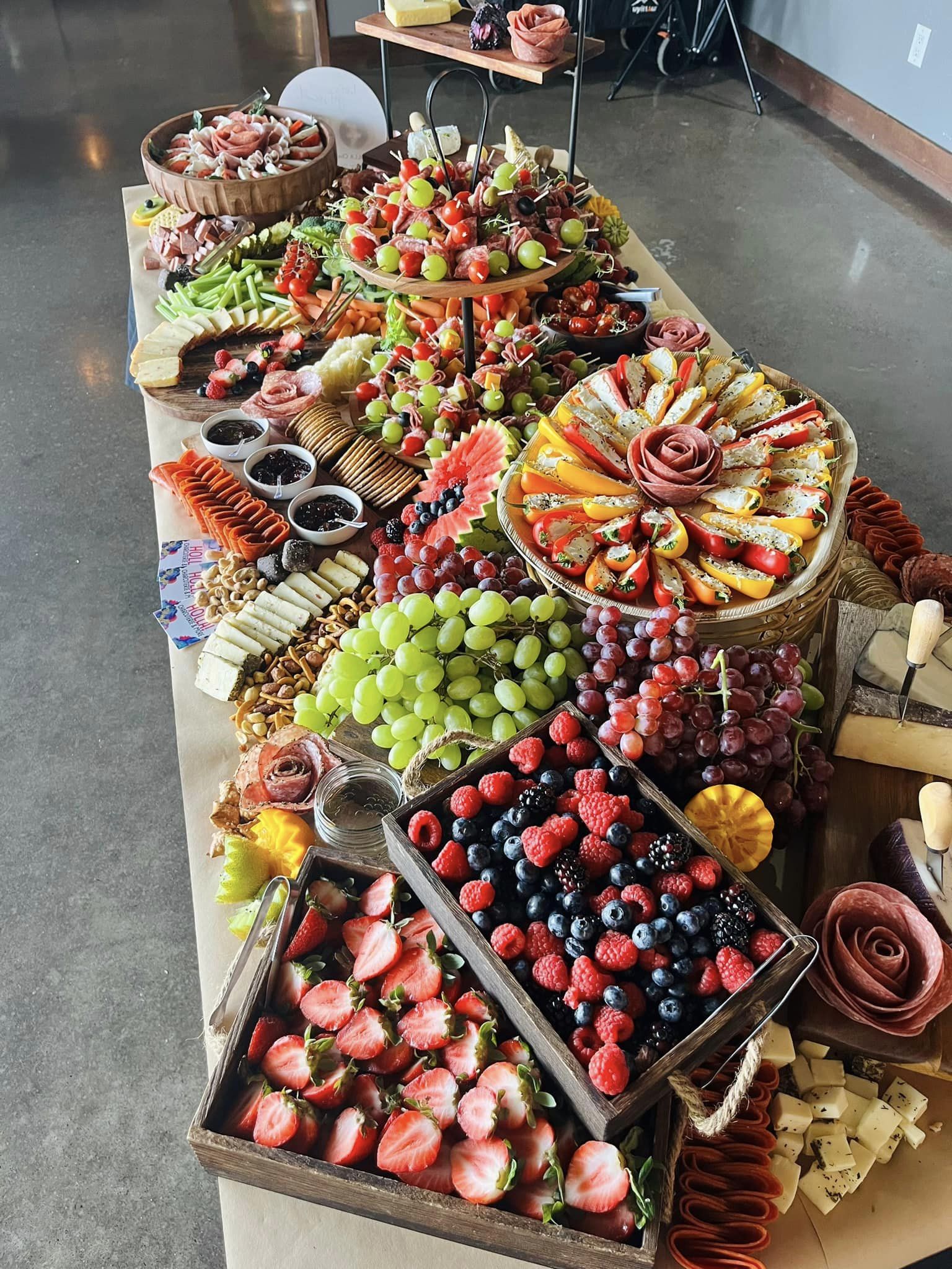 A vibrant buffet displays an array of fresh fruits, cheeses, and meats arranged artfully on rustic wooden platters, set in bright daylight.