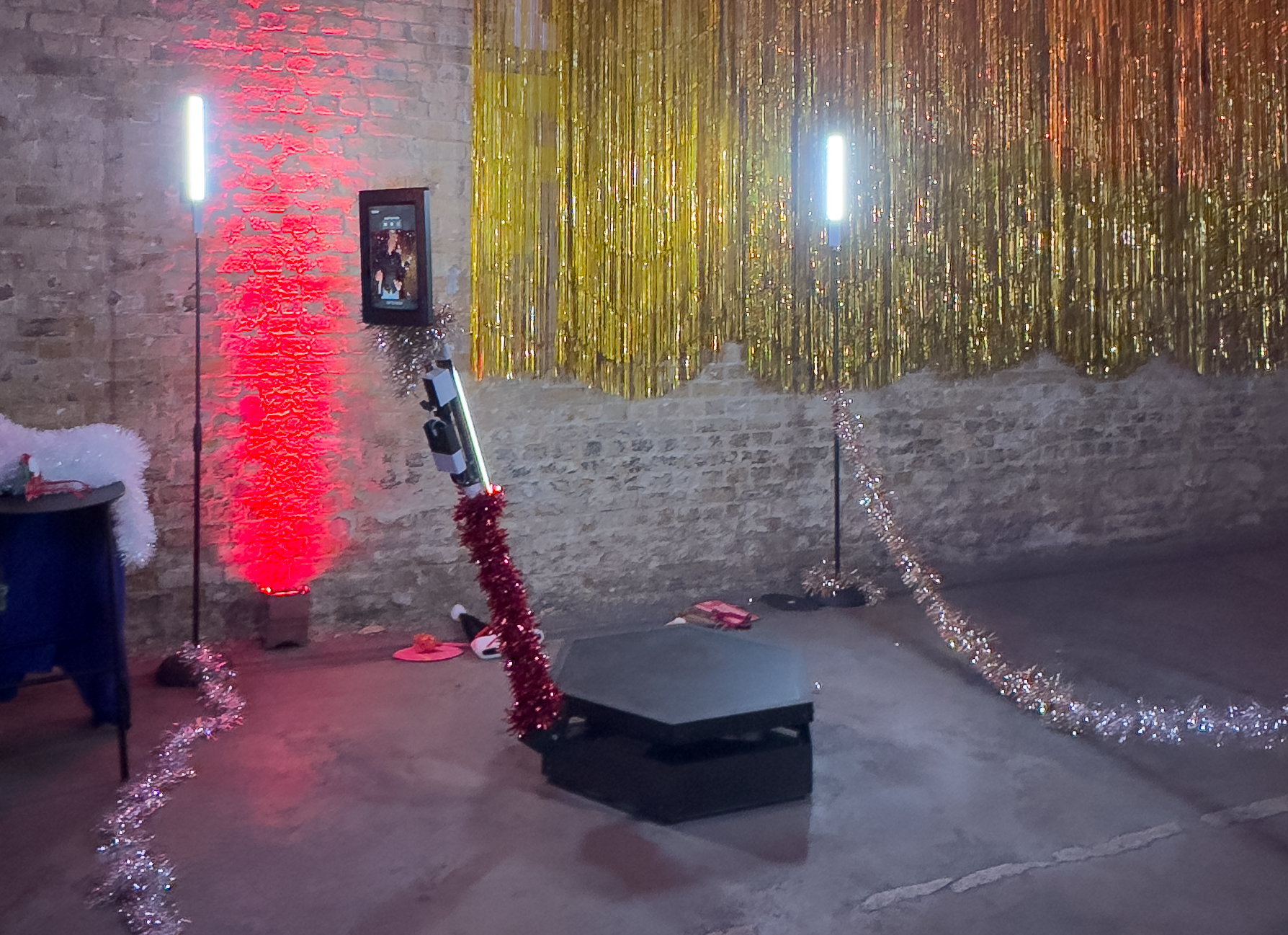 A cozy event space features vibrant red and gold decorations, with a shiny backdrop and a sleek black hexagonal podium, accented by twinkling tinsel, creating a festive atmosphere.