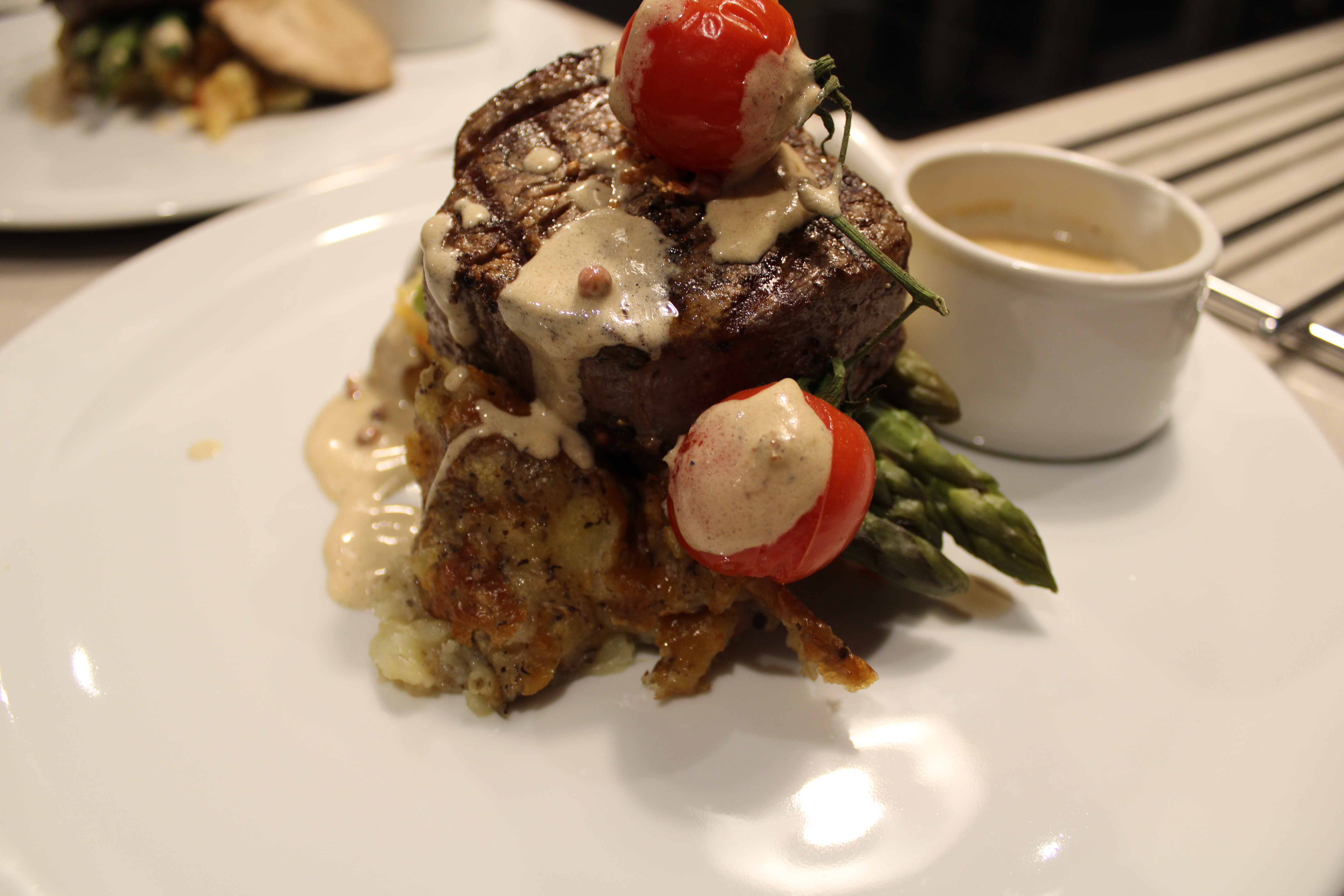 A perfectly cooked filet mignon topped with creamy sauce and vibrant cherry tomatoes, garnished with asparagus, on a white plate, exudes elegance.