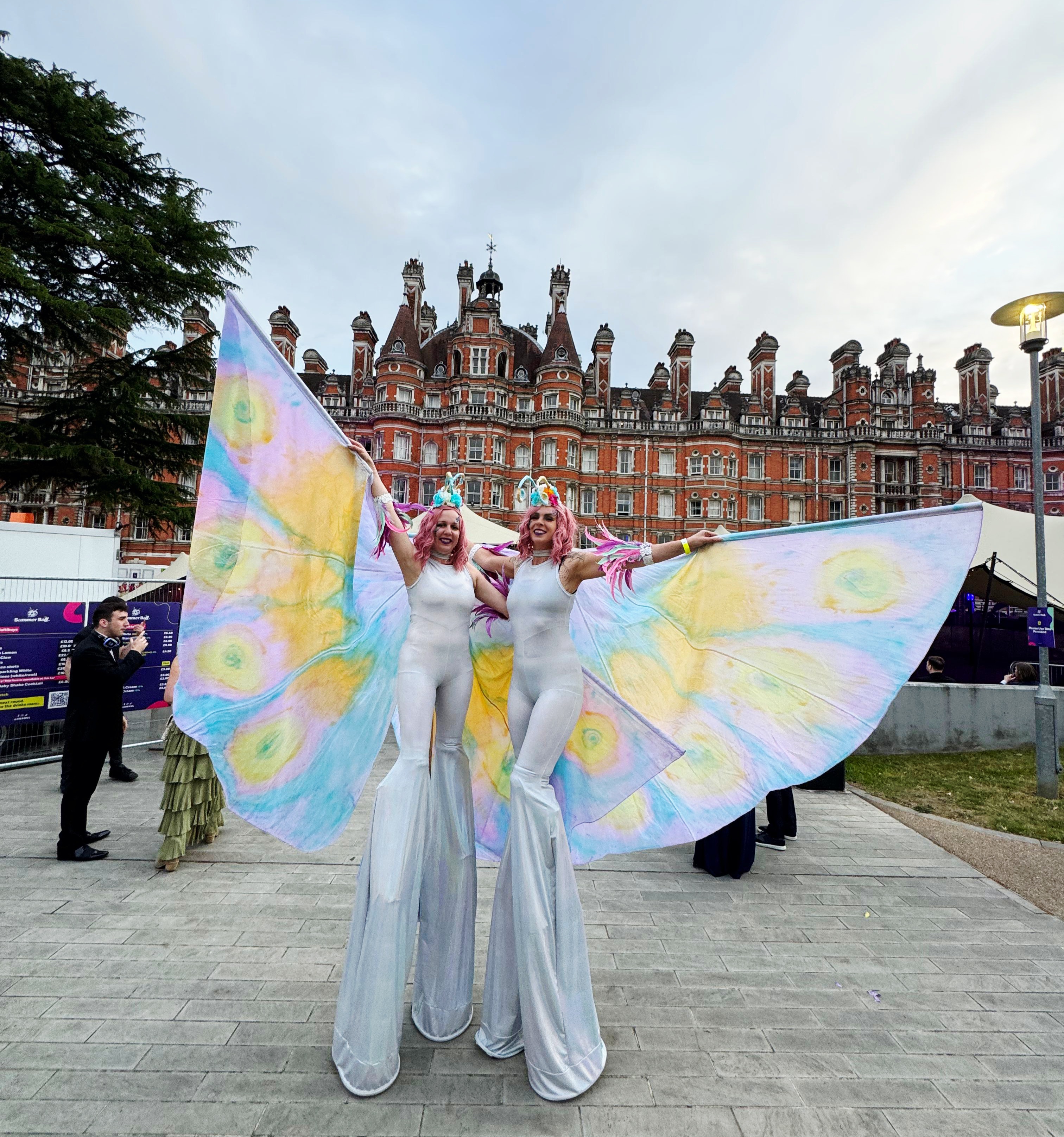 In a festive setting, cheerful performers in vibrant costumes, including gold and red, engage with passersby amid urban decor.