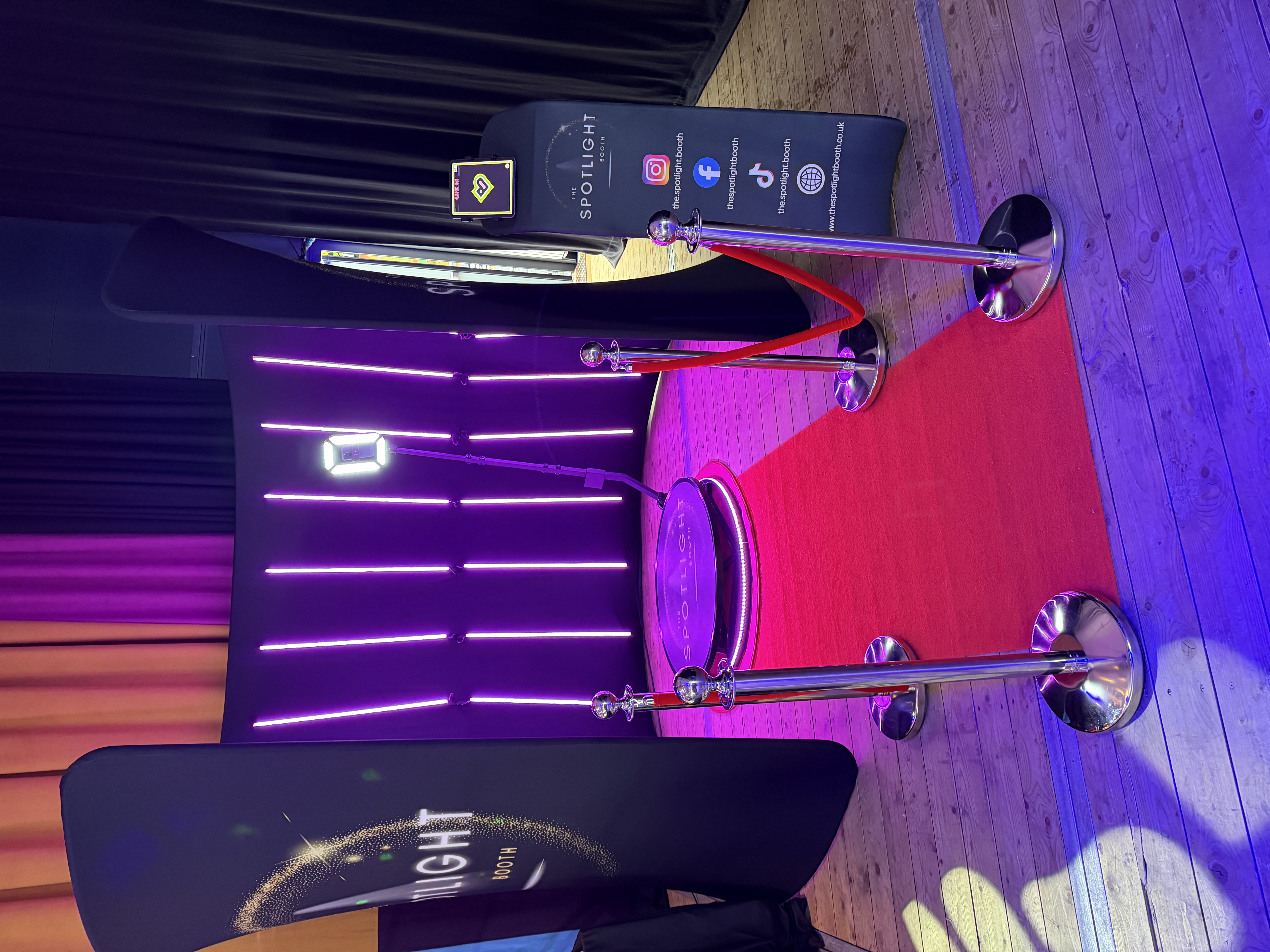 Neon-lit Spotlight Booth with red carpet, chrome stanchions, curved LED backdrop, and polished ring light, styled for premium event photography.