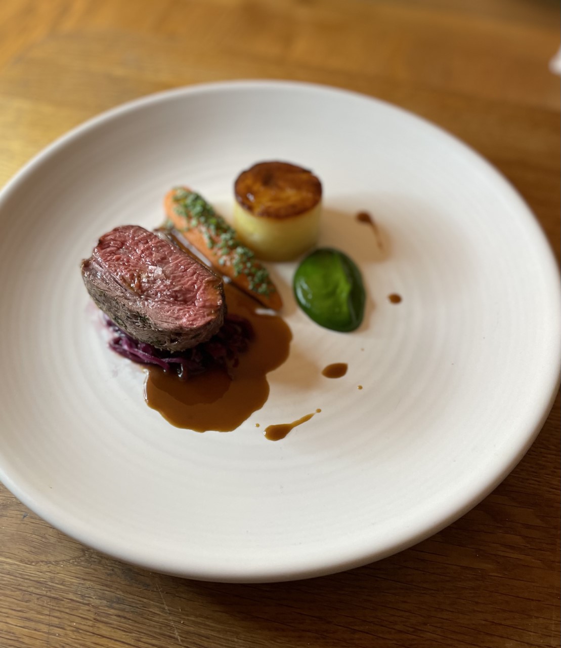 A perfectly seared beef filet sits atop a bed of vibrant purple cabbage with artful carrots and sauce, all presented on a rustic plate.