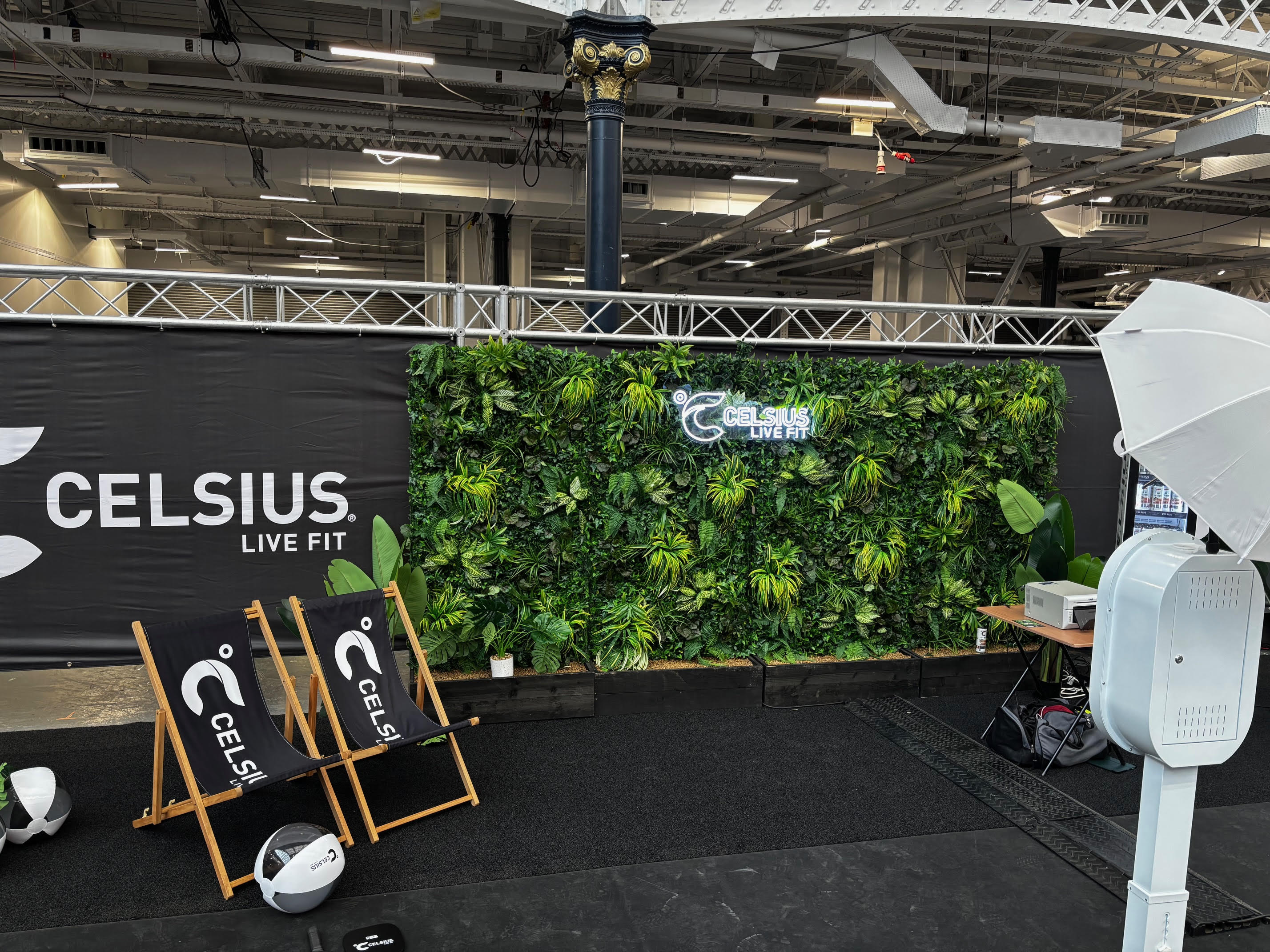 A vibrant green wall features lush foliage, complementing sleek black deck chairs and a minimalist ambiance, illuminated for a fresh, energetic vibe.