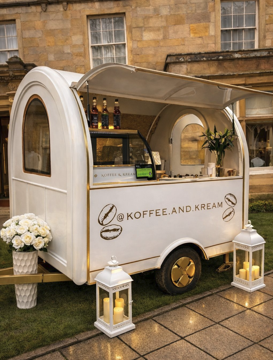 A chic vintage coffee trailer features gold accents, soft white flowers in a textured vase, and glowing lanterns beside polished paths, evoking warmth.