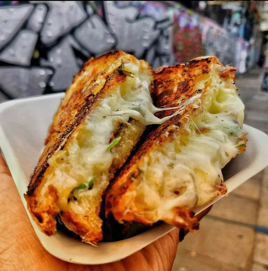 Golden-brown grilled cheese sandwiches with gooey mozzarella, neatly arranged in a hand, set against a vibrant graffiti backdrop.