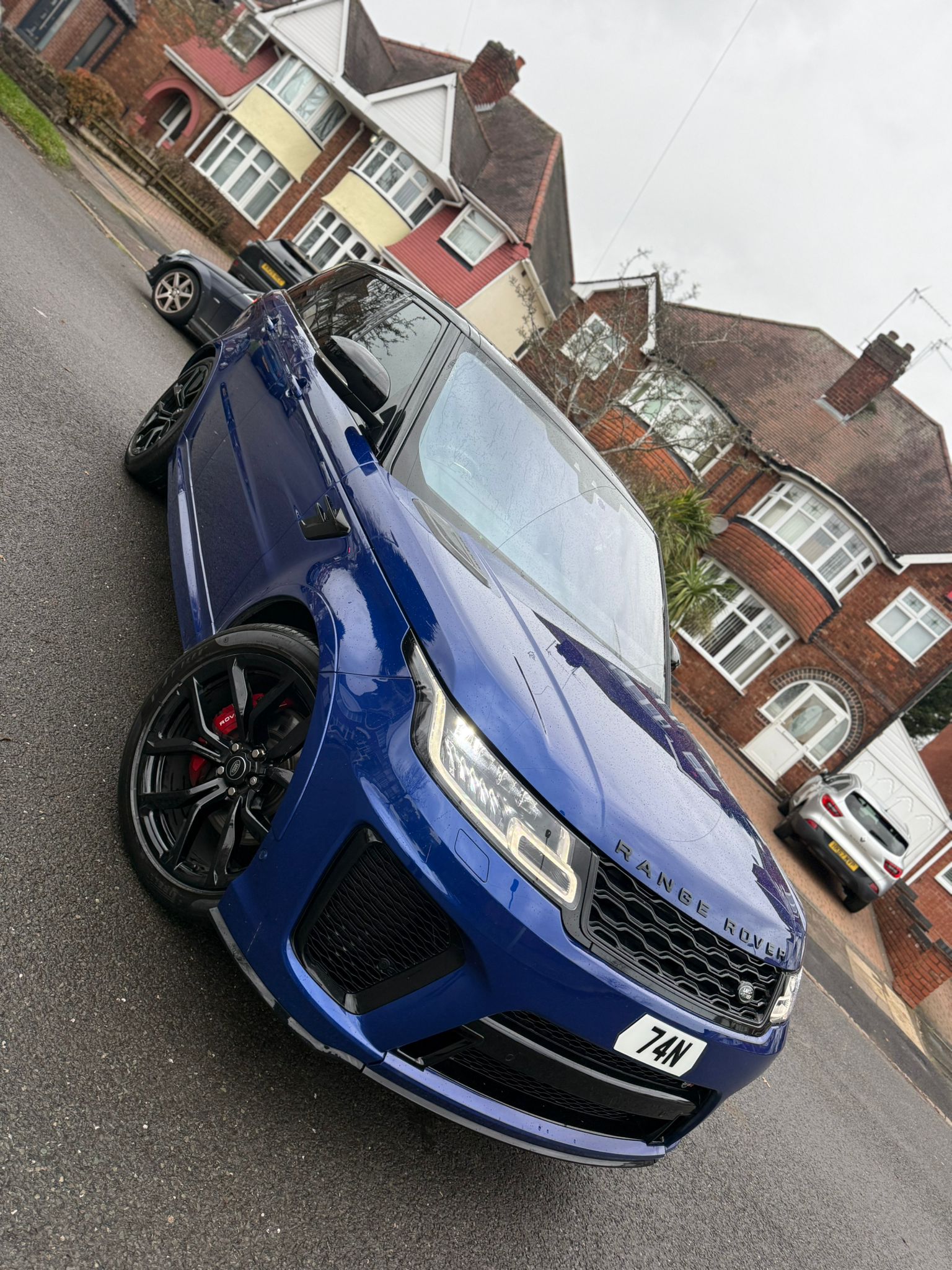 A sleek blue Range Rover parked on a residential street, showcasing its bold lines and shiny black alloy wheels under overcast skies.