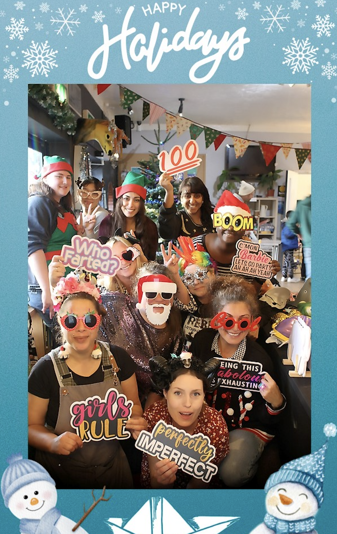 Cheerful holiday photo booth at a Christmas catering party, with smiling guests holding playful props under warm indoor lighting.