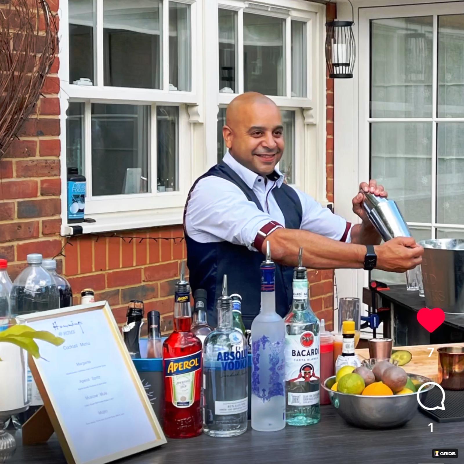 A skilled bartender in a sleek vest mixes drinks at an outdoor bar, showcasing colorful bottles and fresh fruits, with bright daylight ambiance.