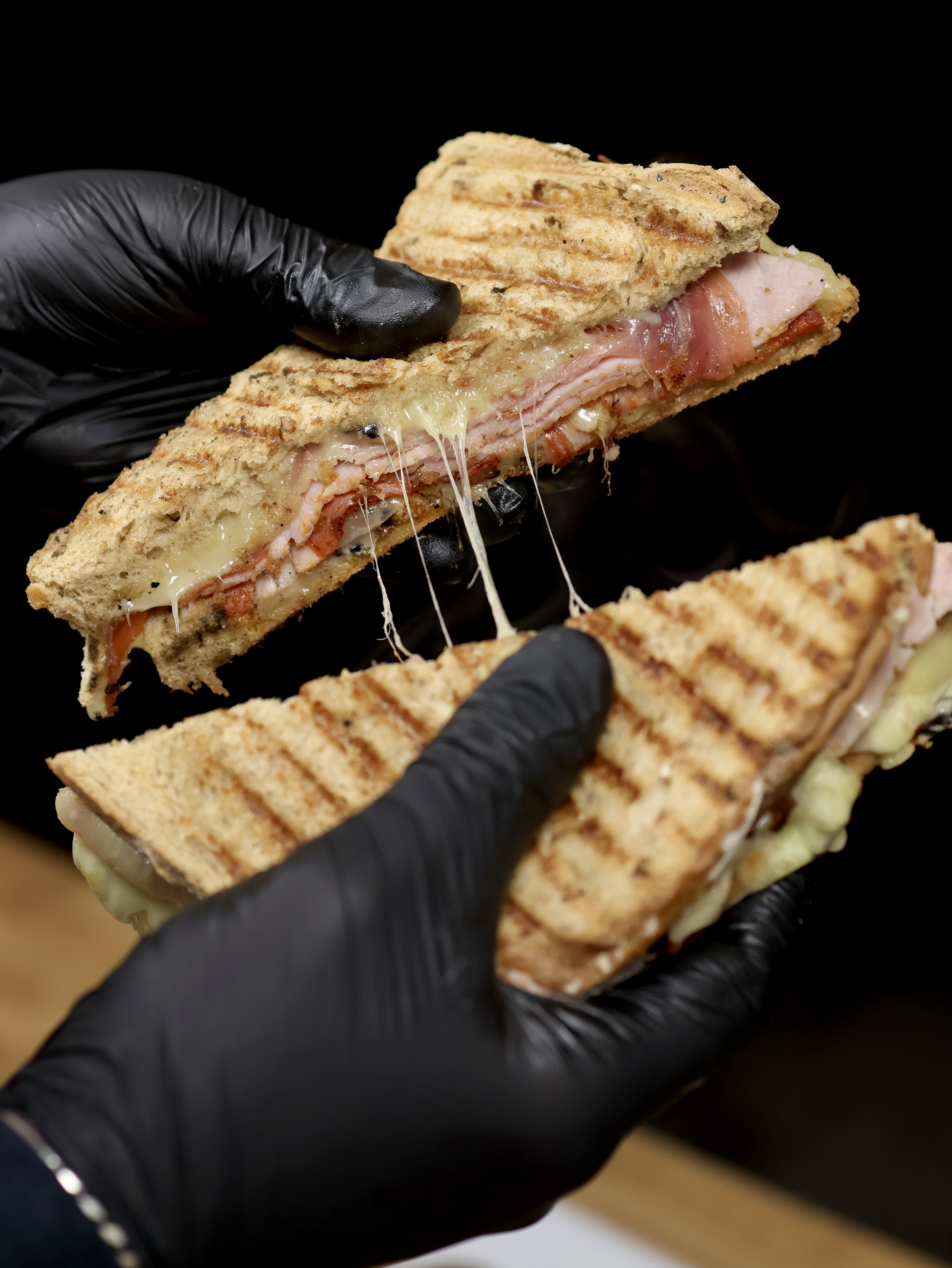 Grilled sandwiches ooze with melted cheese and layers of ham, set against a simple dark backdrop, showcasing quality and craft in catering.
