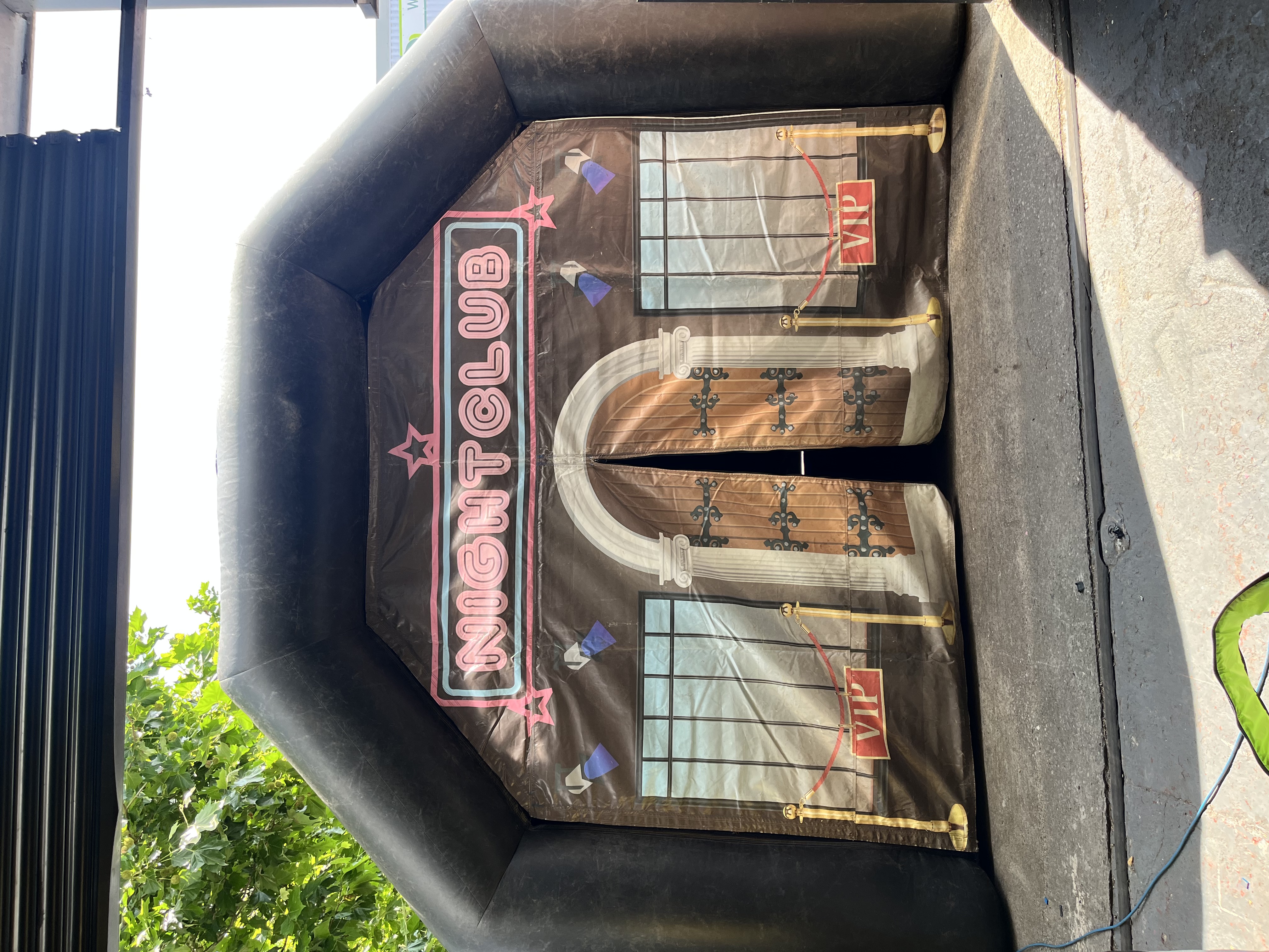 Black inflatable night-club entrance with neon-pink signage, VIP ropes and printed arched doors, set outdoors in bright daylight.