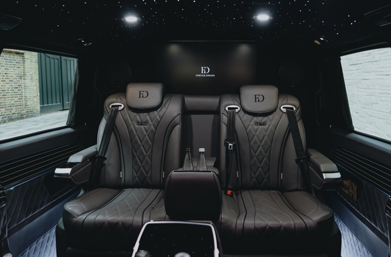Luxury black leather van interior with quilted seats, FD branding, starry ceiling lights, and polished bottle holders, moody and sleek.
