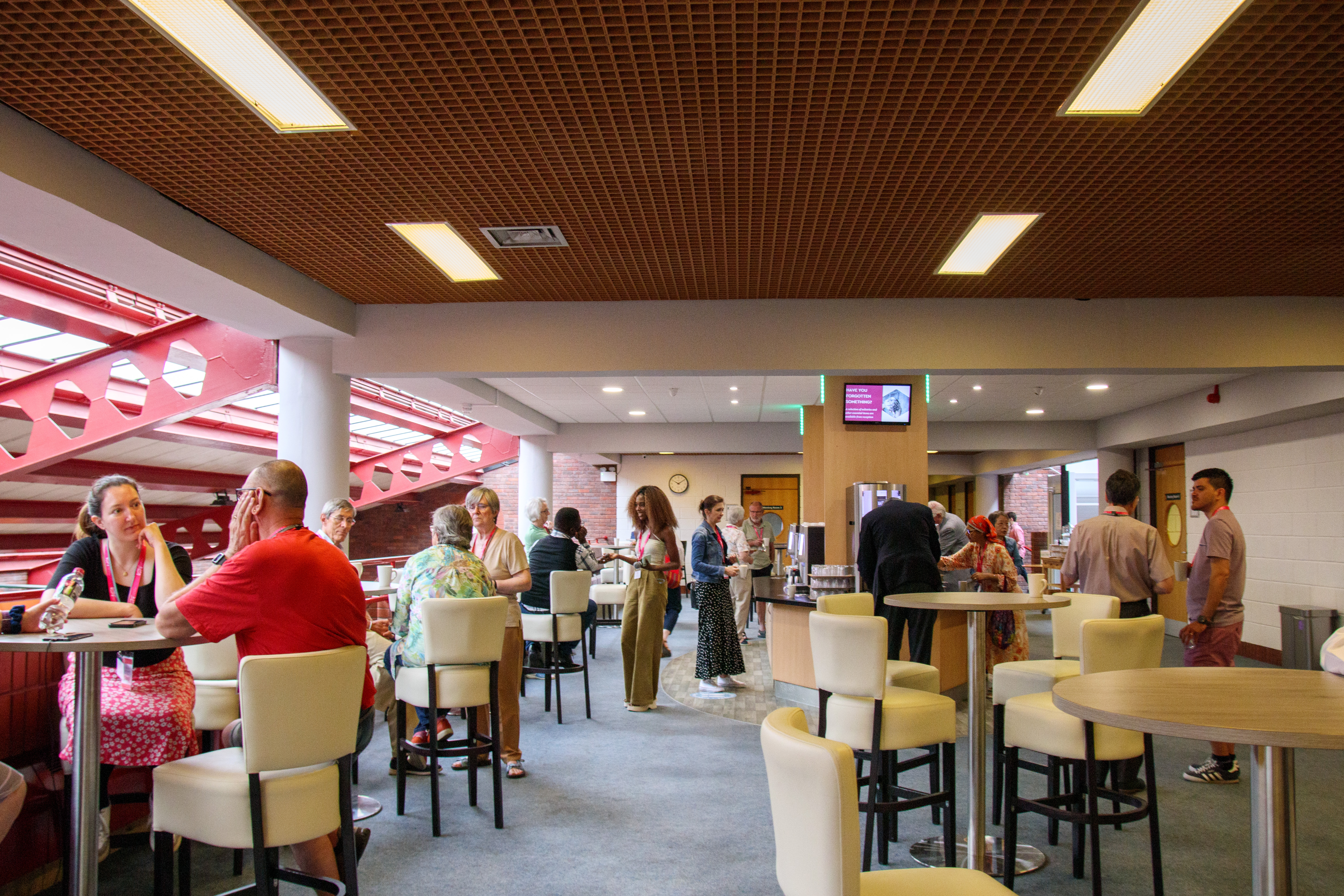 Bright lobby catering area with round tables, cream barstools, polished coffee station, and warm ceiling lights, lively mingling crowd.