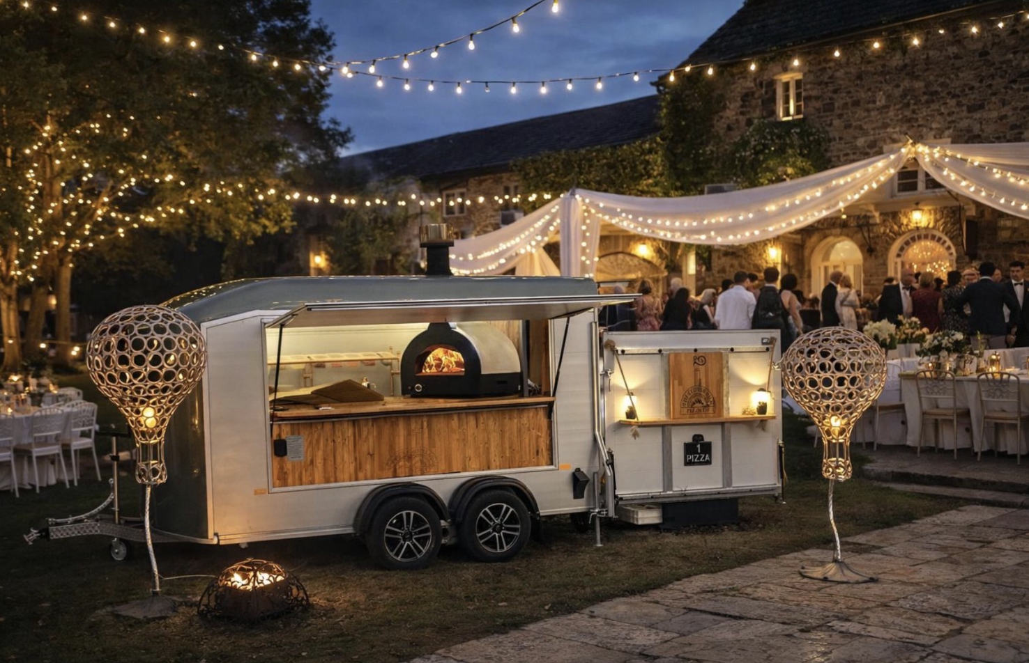Under warm, twinkling lights, a vintage pizza van with a wood-fired oven showcases rustic wooden accents, adding charm to a festive outdoor event.