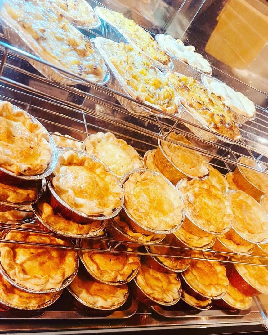 A warm display case filled with golden-brown pies, arranged neatly in a stacked manner, emphasizes quality catering with crispy crusts.