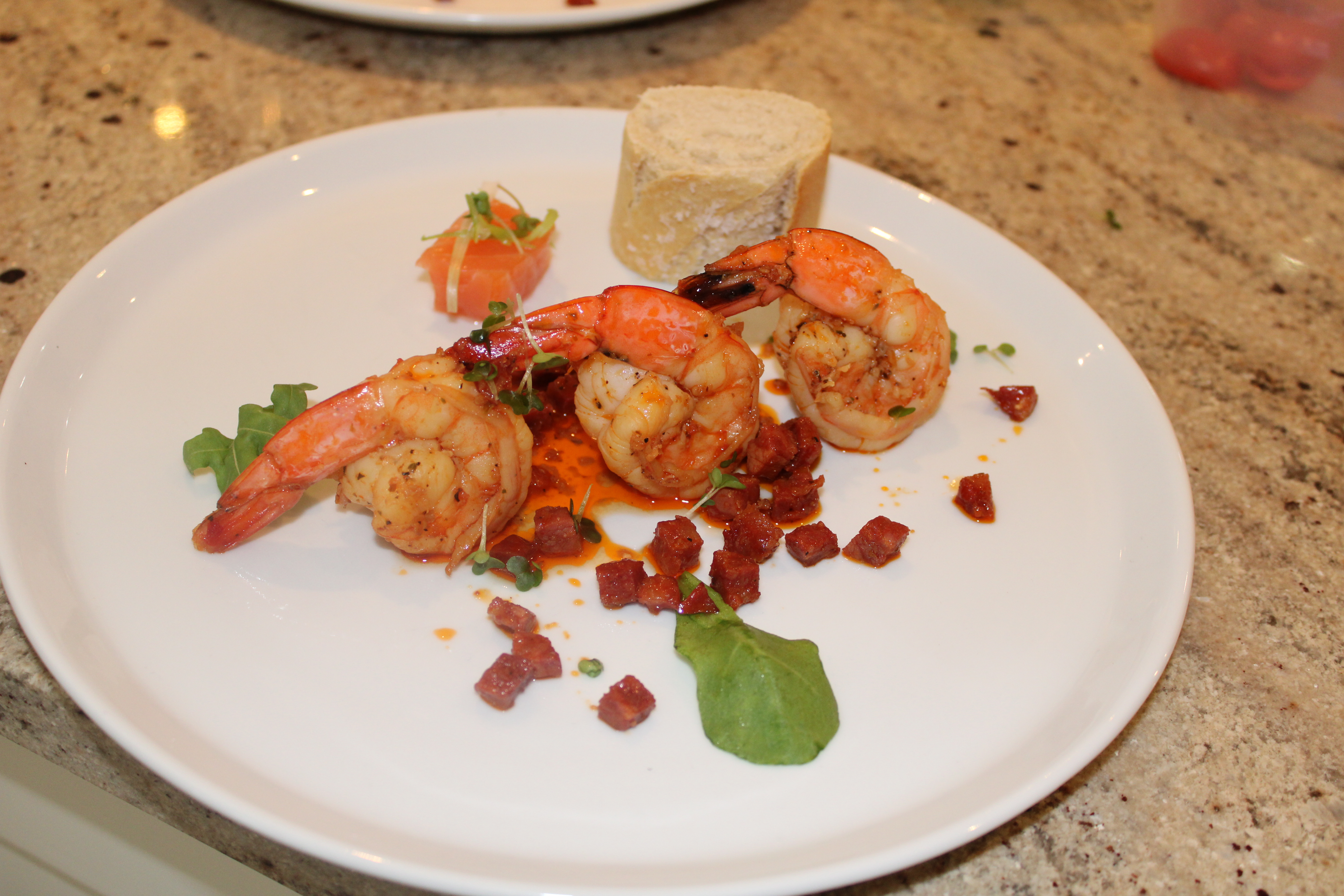 Succulent grilled shrimp with vibrant orange hues are elegantly arranged alongside crispy chorizo, garnished with microgreens and artisanal bread, creating a refined dining experience.