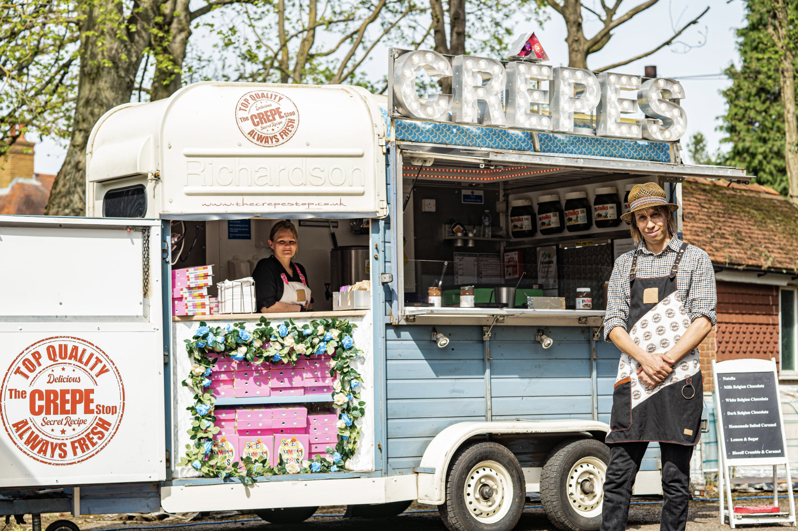 A vintage-inspired crepe van features pastel blue accents, floral decorations, and bright signage, creating a welcoming atmosphere.