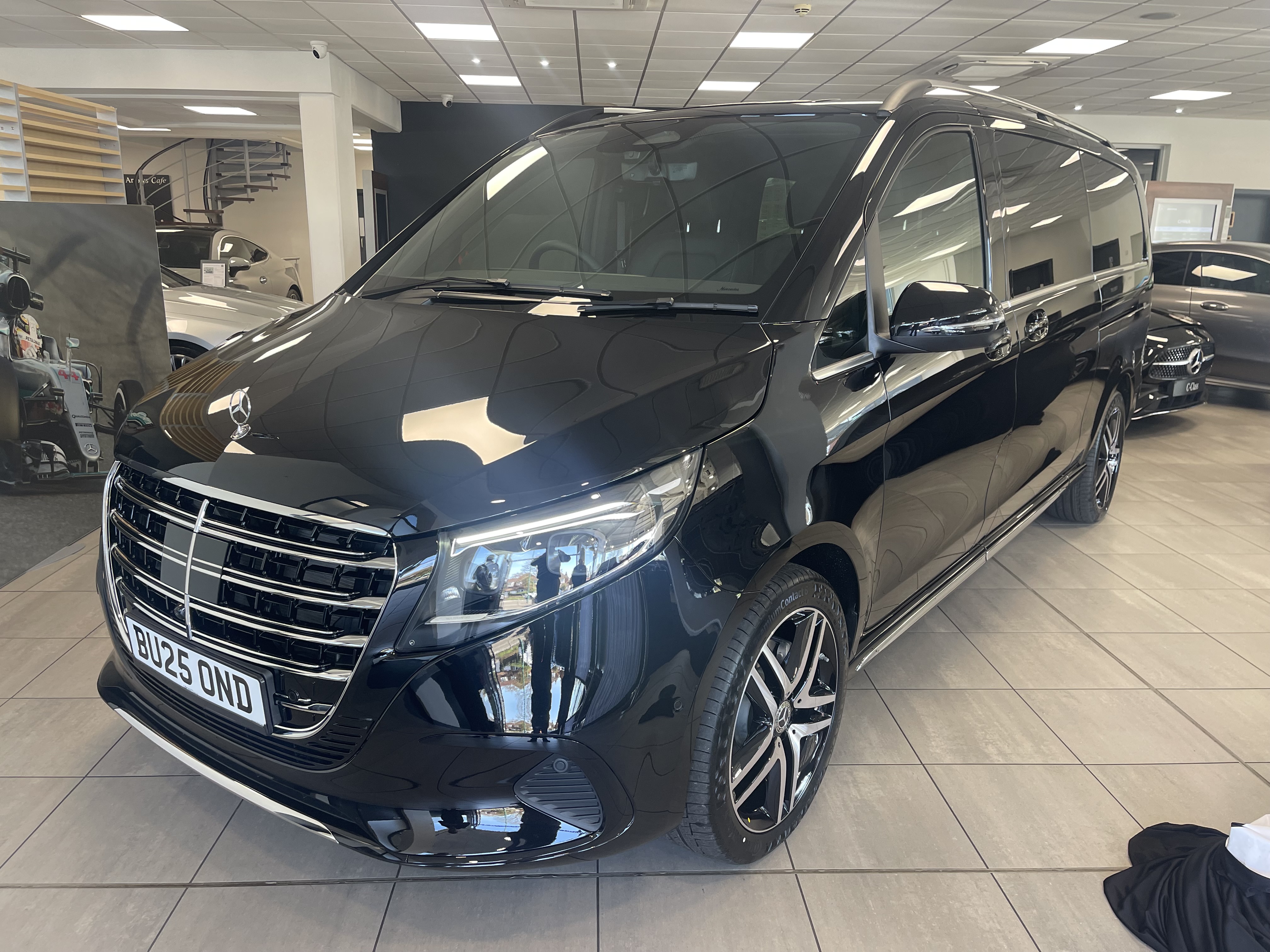 A sleek black Mercedes van is showcased in a bright, modern dealership, featuring polished finishes and stylish rims, exuding luxury.