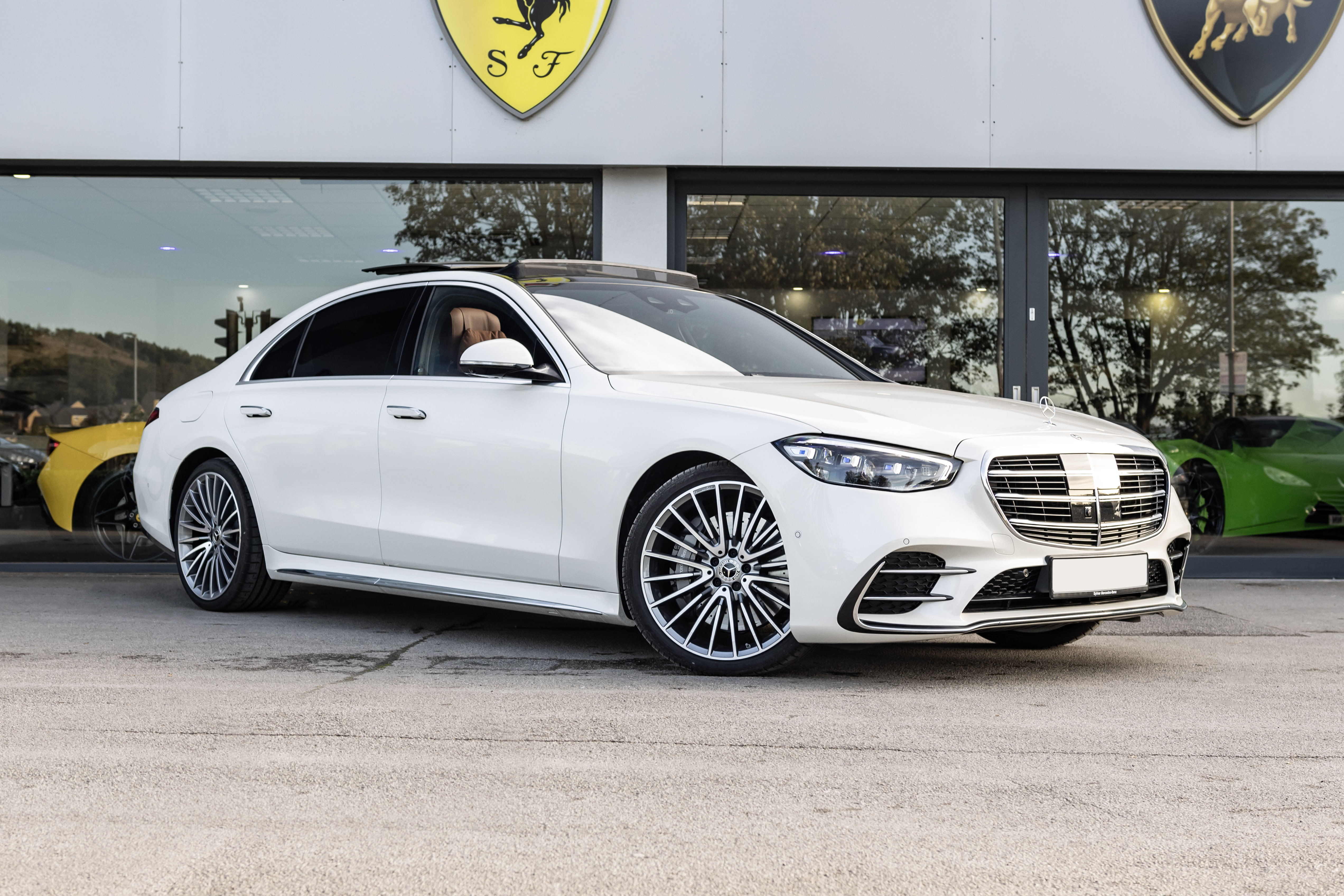 A sleek white luxury sedan with polished alloy wheels is parked outside a modern showroom, showcasing an elegant design and premium finish.