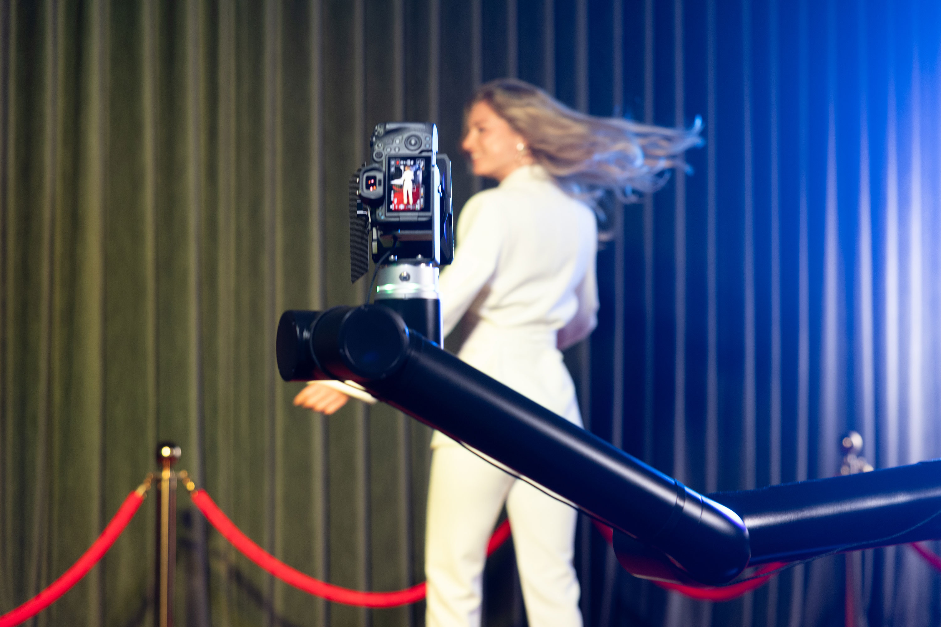 A sleek camera captures a model in a white suit, gracefully turning on a velvet-draped stage, enhancing glamorous event vibes.