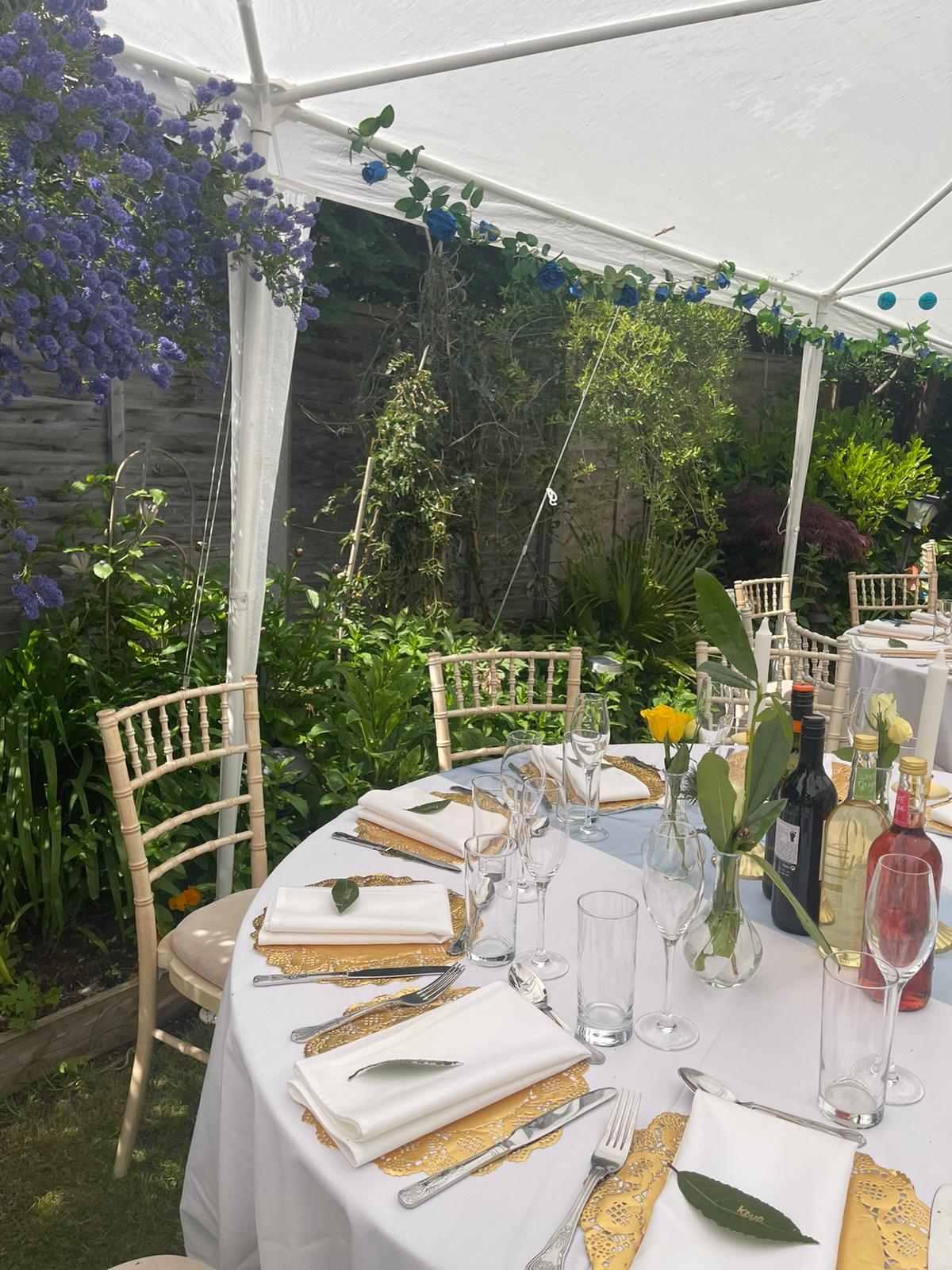 A beautifully arranged outdoor table features crisp white linen, elegant golden placemats, and vibrant floral accents, all bathed in natural sunlight.