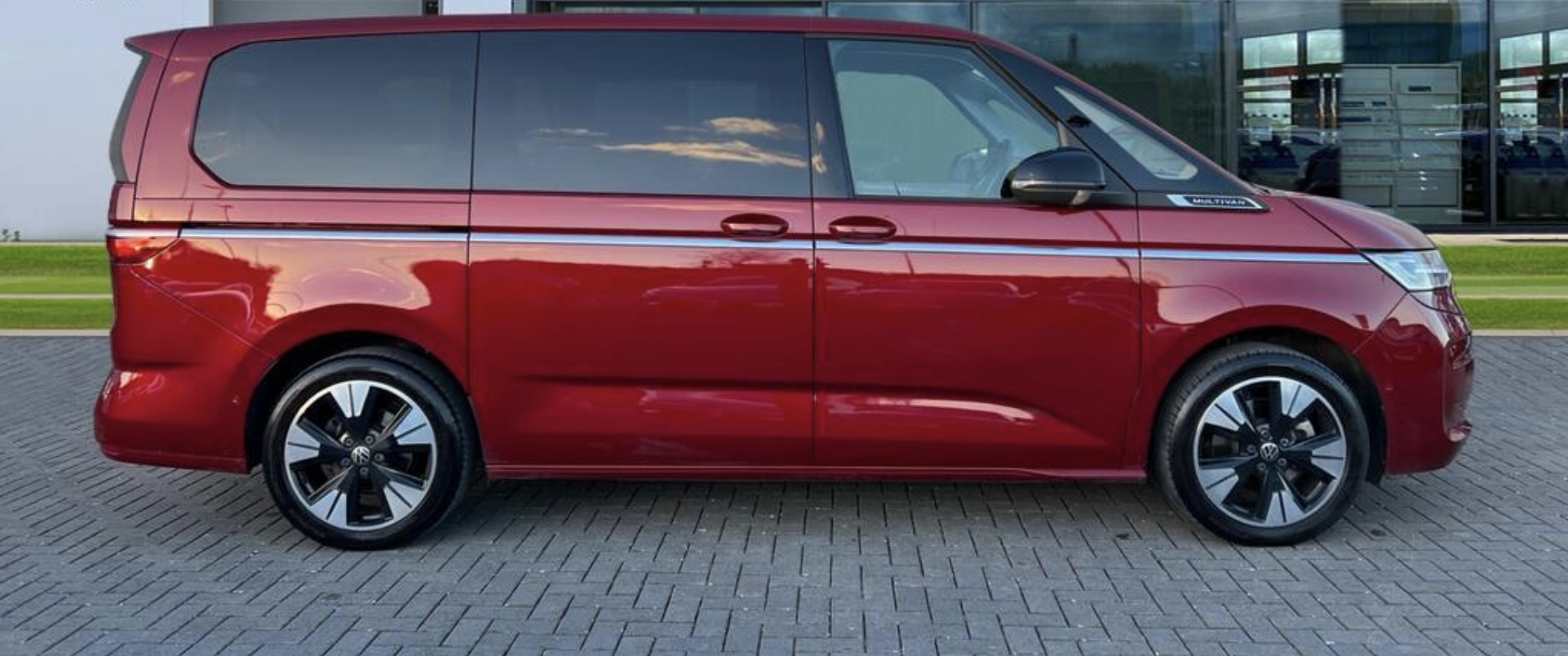 A sleek red van with chrome accents shines against a polished stone pavement, showcasing modern design and spaciousness perfect for family trips.