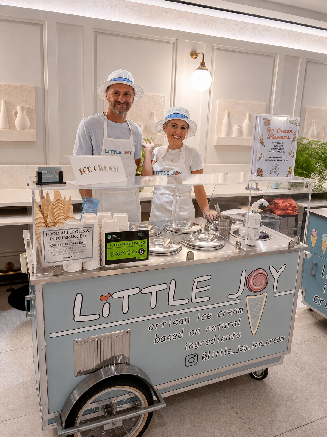 A charming ice cream cart, “Little Joy,” features shimmering metal tubs and natural ingredient signage, complemented by cheerful staff, evoking a lively, inviting atmosphere.