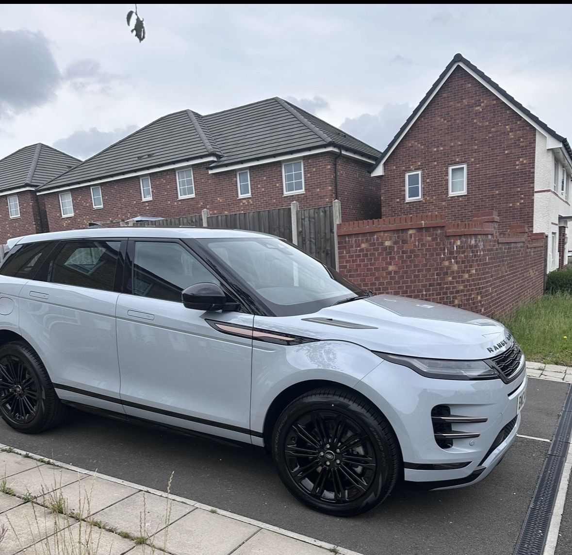 Light blue Range Rover SUV parked curbside outside brick homes, black wheels gleaming in soft daylight, clean upscale street scene.