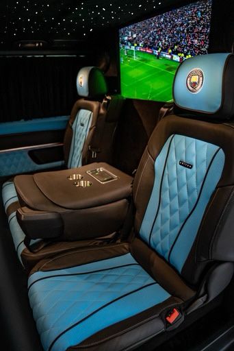 Luxurious leather seats in rich blue and black hues feature diamond stitching, amid ambient lighting with a wall-mounted screen, perfect for upscale travel.
