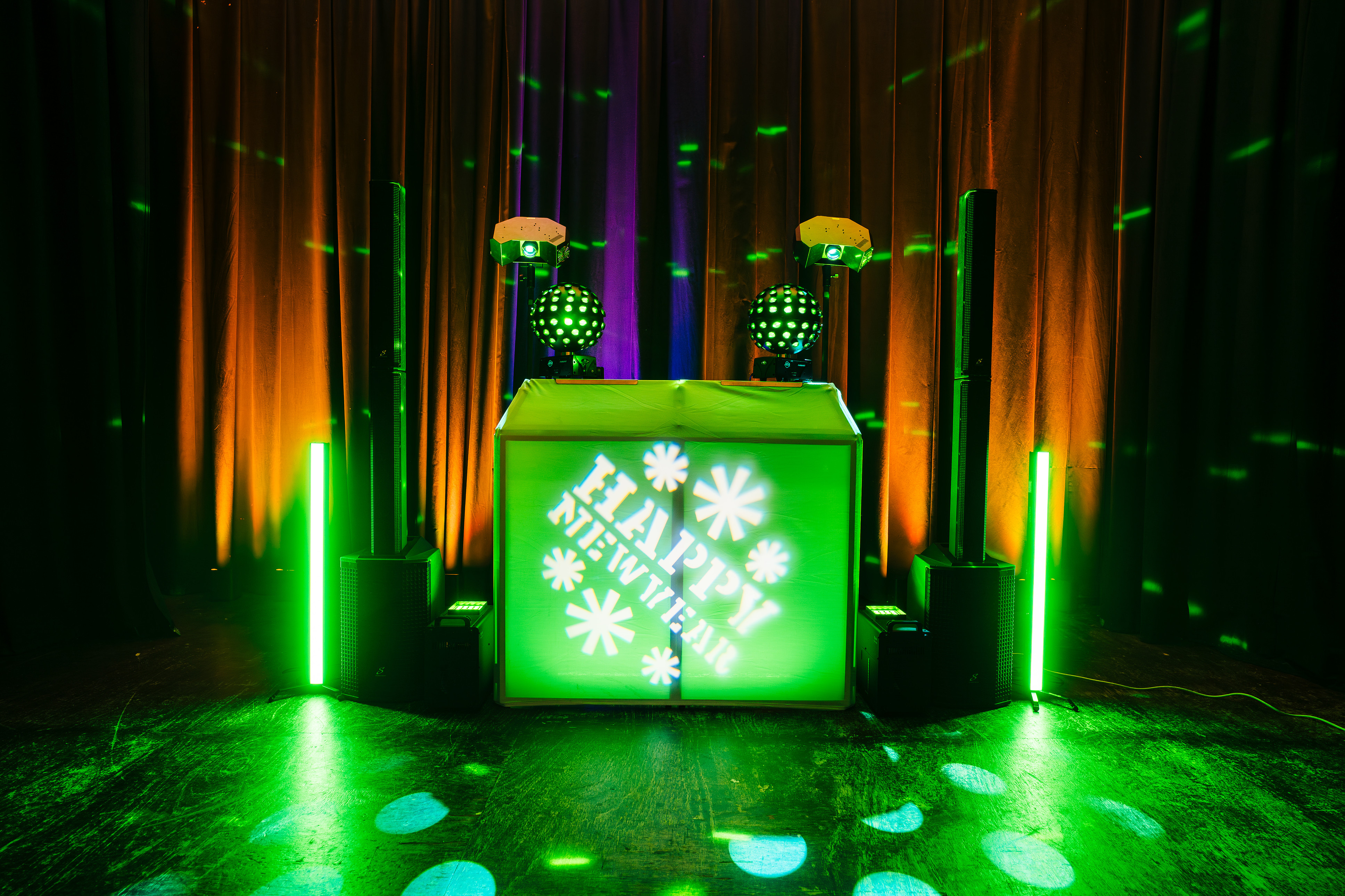 Neon-green DJ booth with speaker towers, moving lights, and orange-purple drapes creates a sleek, high-energy event catering vibe.