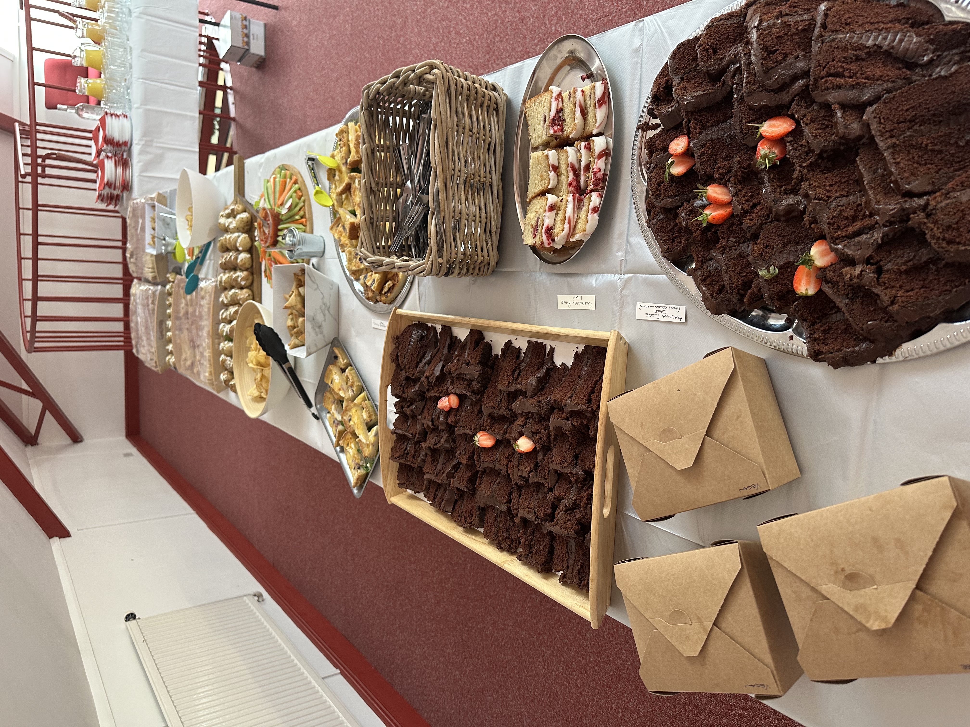 A vibrant buffet features rich chocolate cake, delicate pastries, and fresh veggies, beautifully arranged with polished glassware and warm lighting.