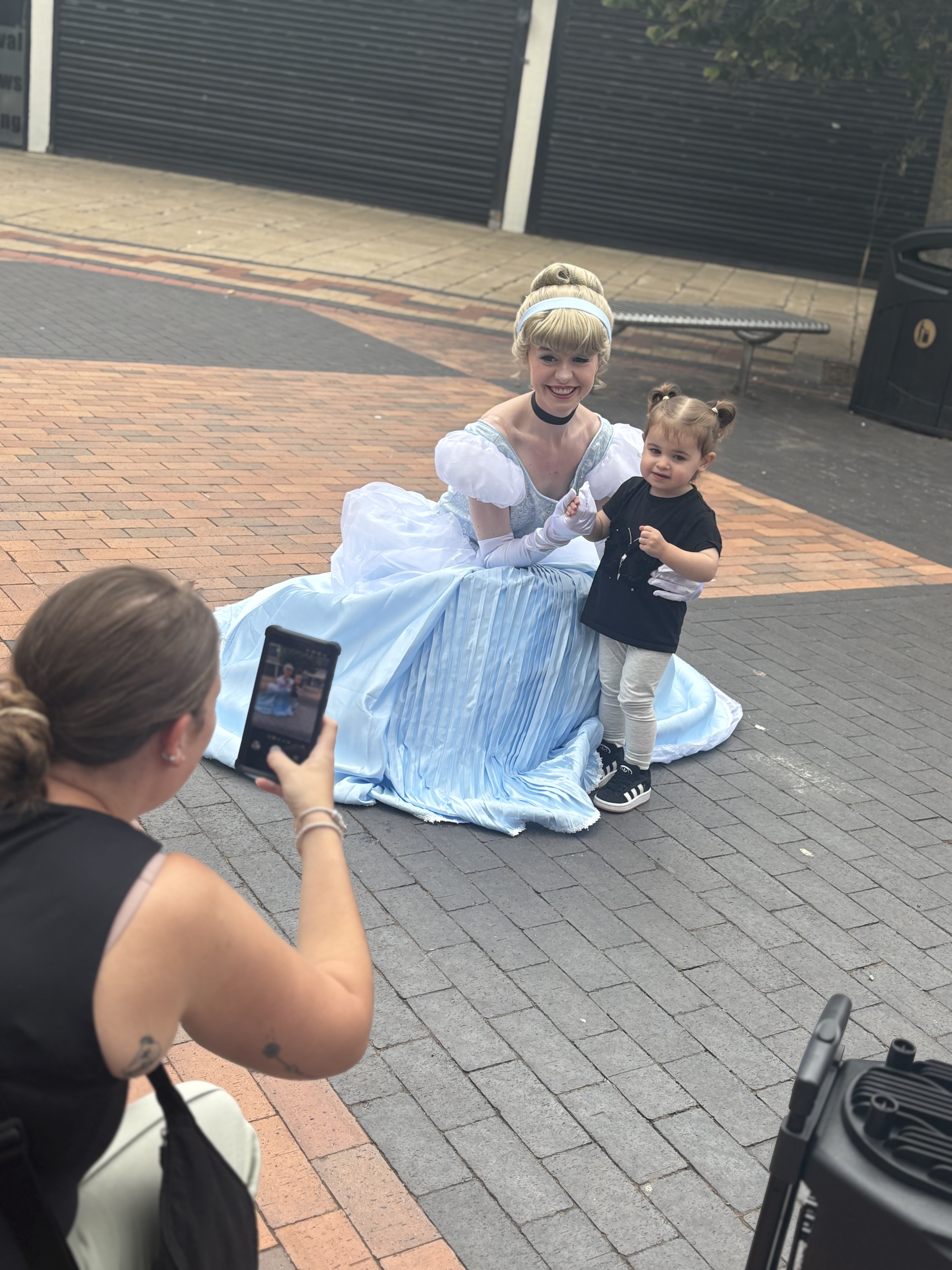 A costumed character in a flowing blue gown kneels with a young girl on textured pavement, capturing a joyful moment amid relaxed outdoor vibes.