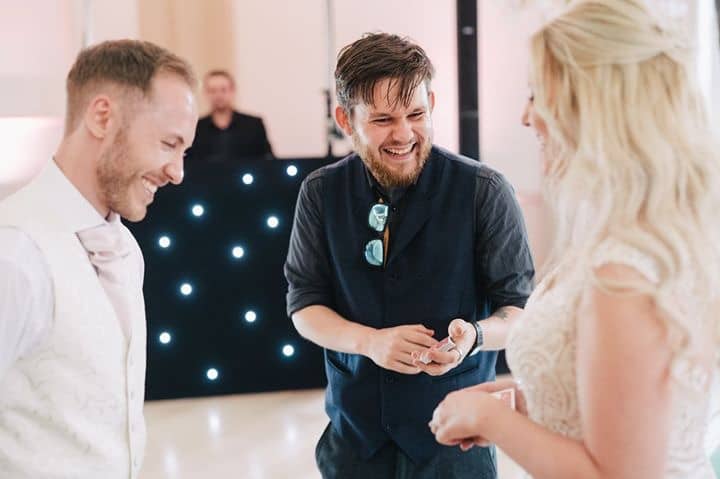A joyful moment unfolds with two men in formal attire and a woman in a lace dress, illuminated by soft ambient lighting, creating an engaging atmosphere.